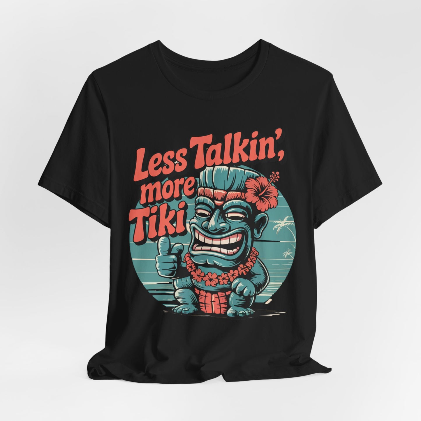 The Tiki Vibes Graphic Tiki T-Shirt - Less Talkin, More Tiki Unisex Shirt is a black tee featuring a colorful cartoon tiki with a flower, giving a thumbs up and “Less Talkin’, More Tiki” in bold orange on a vivid tropical background.