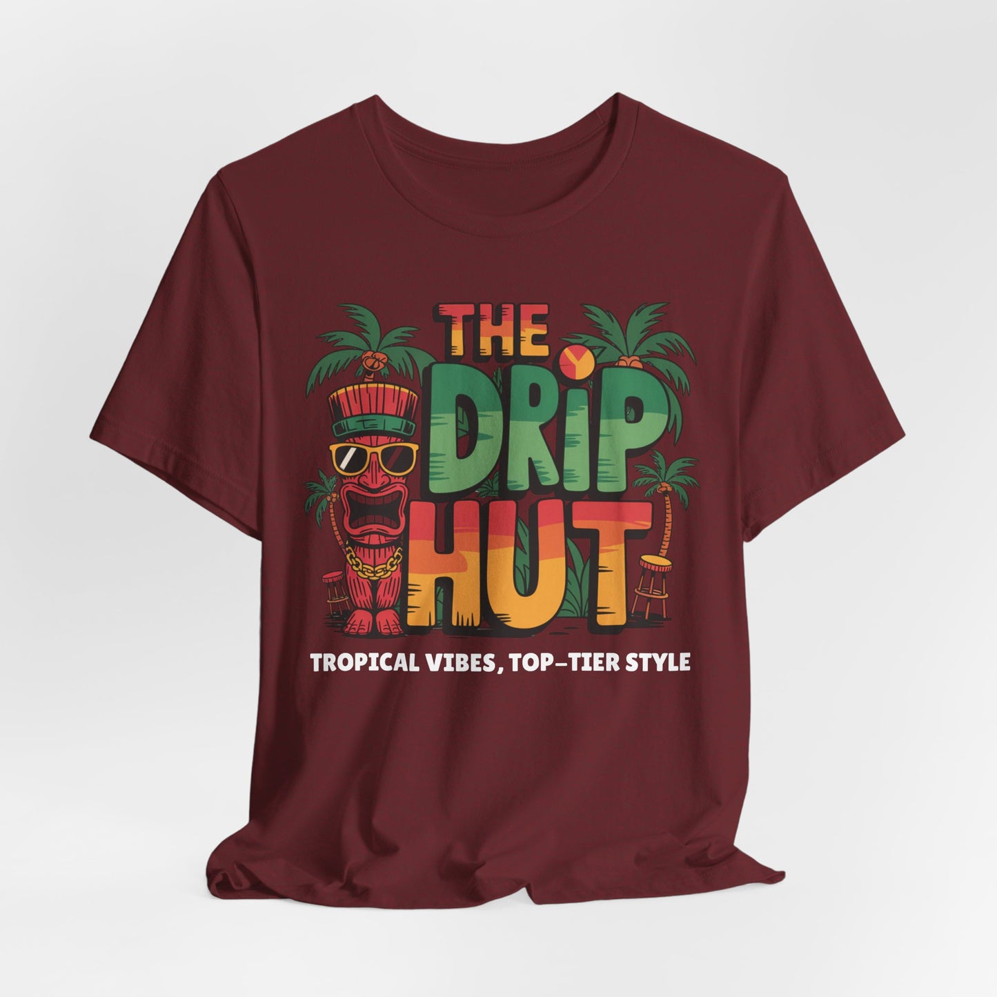 The Tropical Vibes Unisex Tiki T-Shirt - The Drip Hut features colorful The Drip Hut text, tropical palm trees, a tiki mask, and a beach chair with Tropical Vibes, Top-Tier Style below—a perfect tee for standout island style.