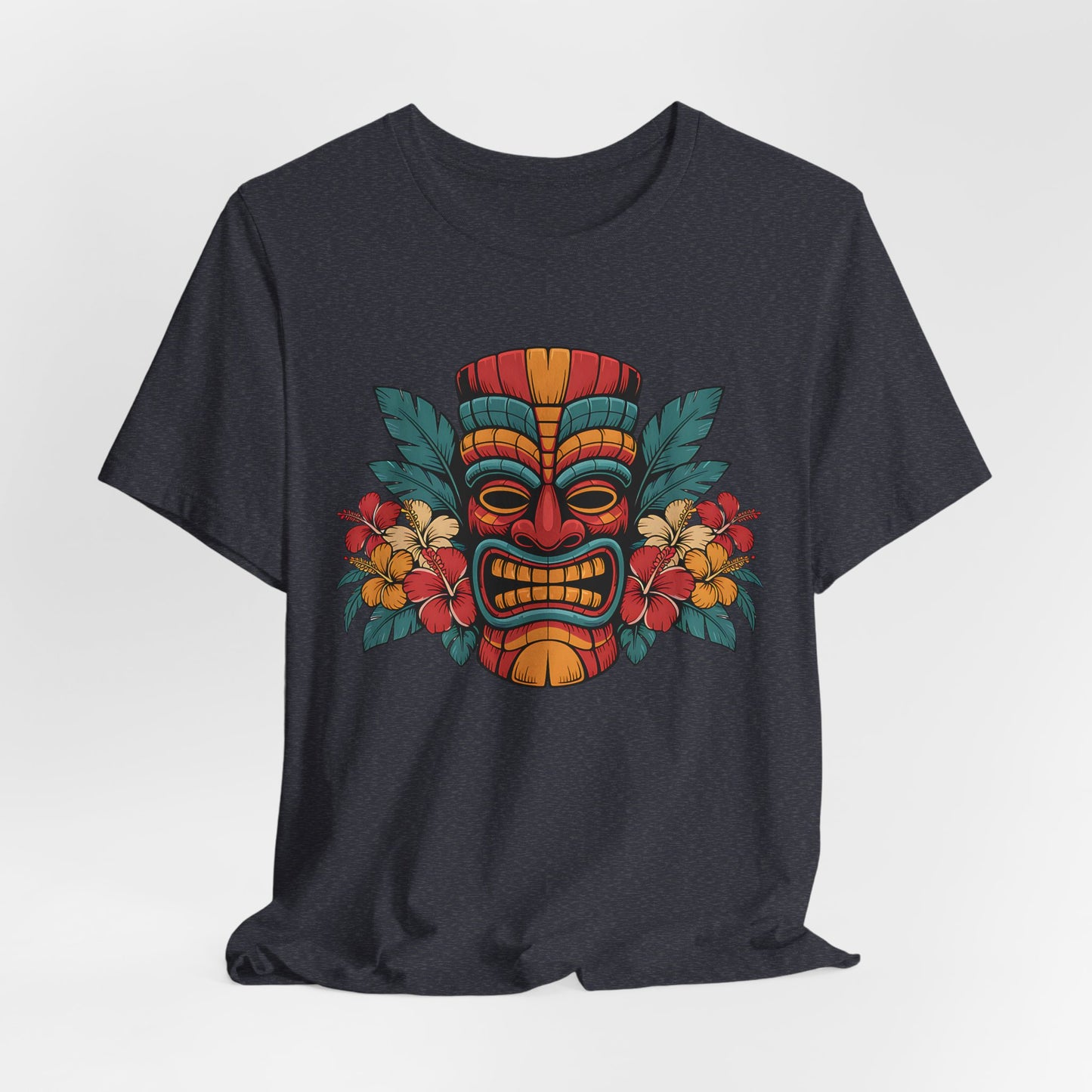 The Tropical Tiki Mask T-Shirt - Unisex Jersey Short Sleeve features a vibrant tiki mask at the center, accented by tropical flowers and leaves in red, yellow, and green for a bold island-inspired look.
