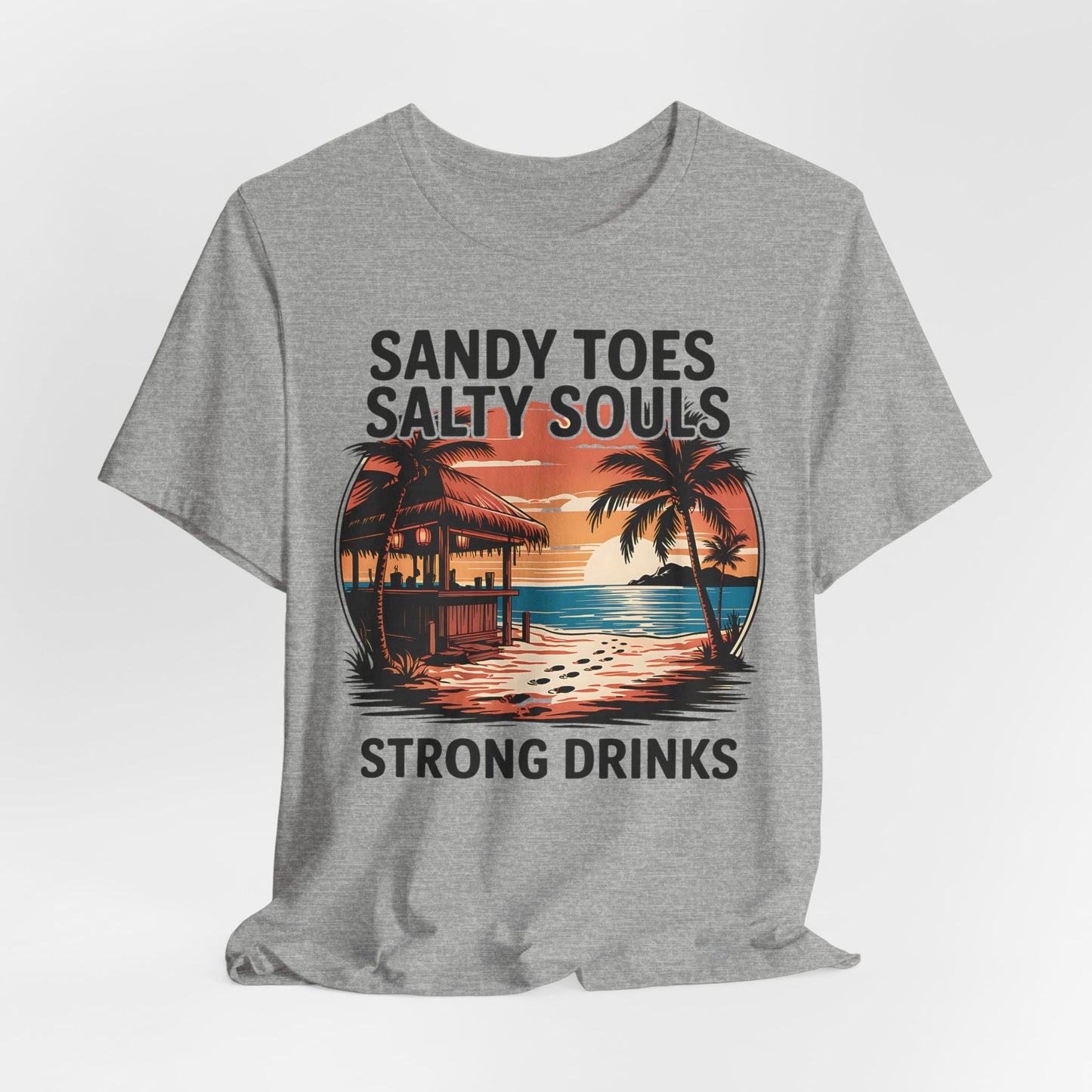 The Sandy Toes Salty Souls Tee is a gray unisex jersey short sleeve featuring a vibrant tropical sunset, palm trees, and hut. Made from soft Airlume combed cotton with the text: Sandy Toes Salty Souls Strong Drinks. Perfect for beach lovers.