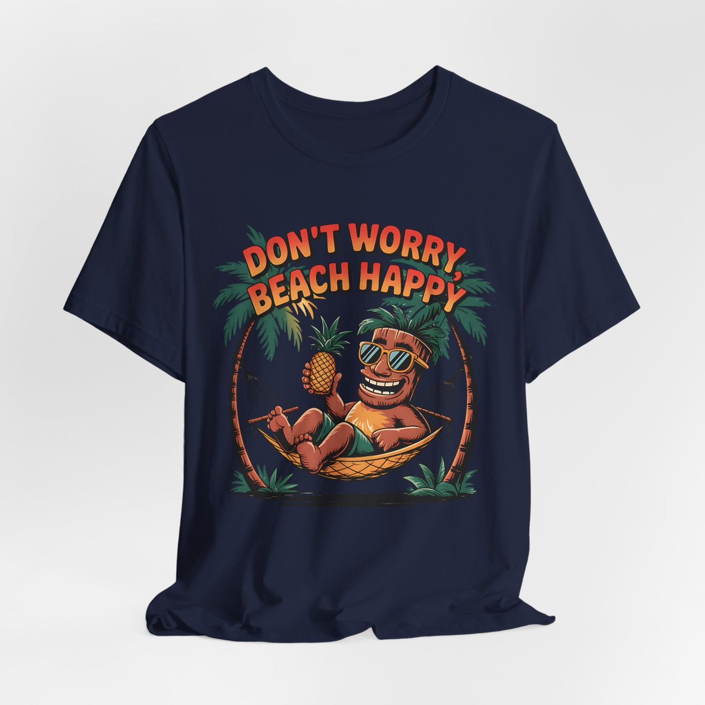 The Dont Worry Beach Happy Tiki T-Shirt is a navy blue unisex jersey tee featuring a grinning tiki with sunglasses and pineapple, framed by palm trees. Perfect for tropical summer vibes, it’s printed with DONT WORRY, BEACH HAPPY in bright orange.