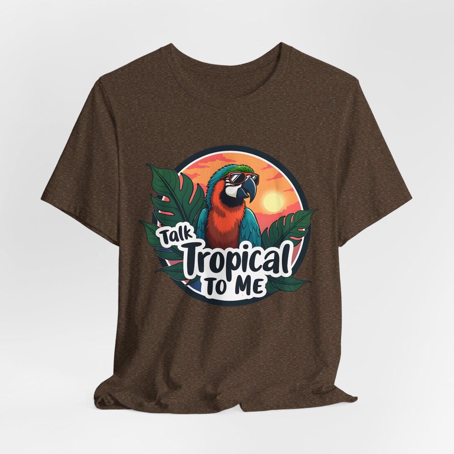 The Tropical Parrot Tee - Talk Tropical to Me Unisex Jersey Short Sleeve Shirt features a vibrant parrot with sunglasses, lush green leaves, and a sunset—ideal for anyone who loves fun tropical vibes.