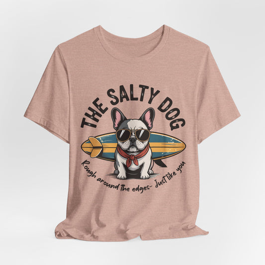 The Salty Dog Unisex Surf T-Shirt is a pink tee with a cartoon French bulldog in sunglasses and a red bandana beside a surfboard. It reads THE SALTY DOG and Rough around the edges—Just like you. Perfect for beach outings!.