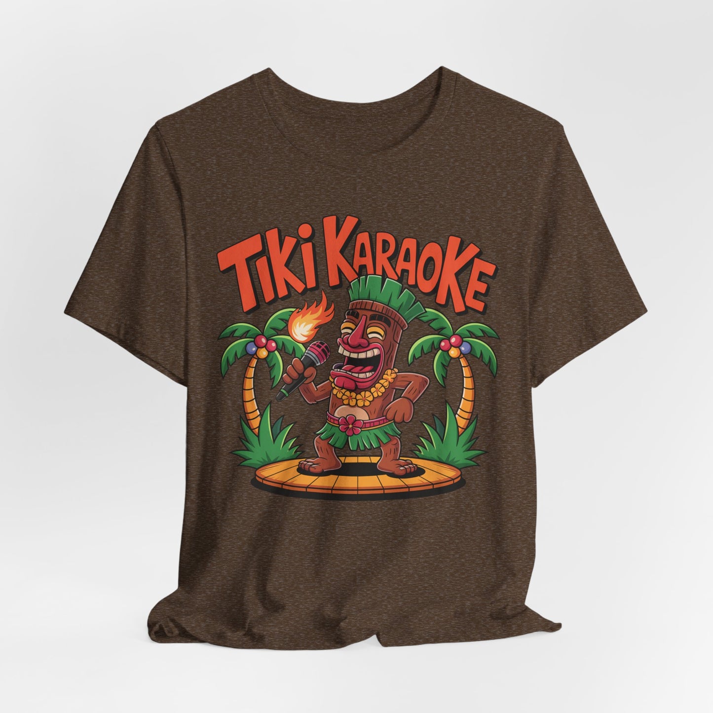 The Tiki Karaoke Unisex Short Sleeve Tiki T-Shirt features a colorful cartoon tiki with a flaming torch on a wooden stage between palm trees and Tiki Karaoke in bold orange letters, perfect for a fun summer vibe.