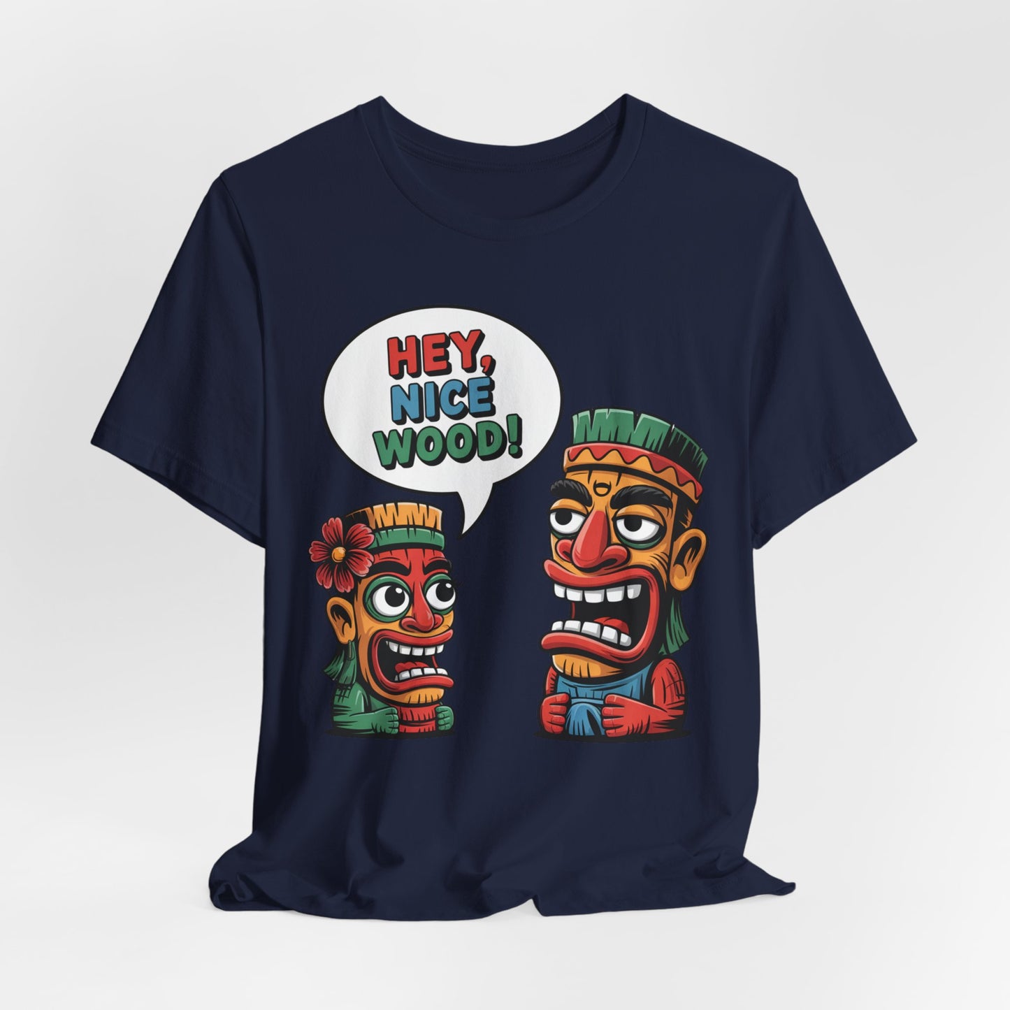 The Tropical Humor Short Sleeve Tiki T-Shirt – Hey, Nice Wood! Graphic is a navy blue unisex tee with two colorful cartoon tiki faces, one with a flower saying HEY, NICE WOOD! in a playful speech bubble to the surprised other.