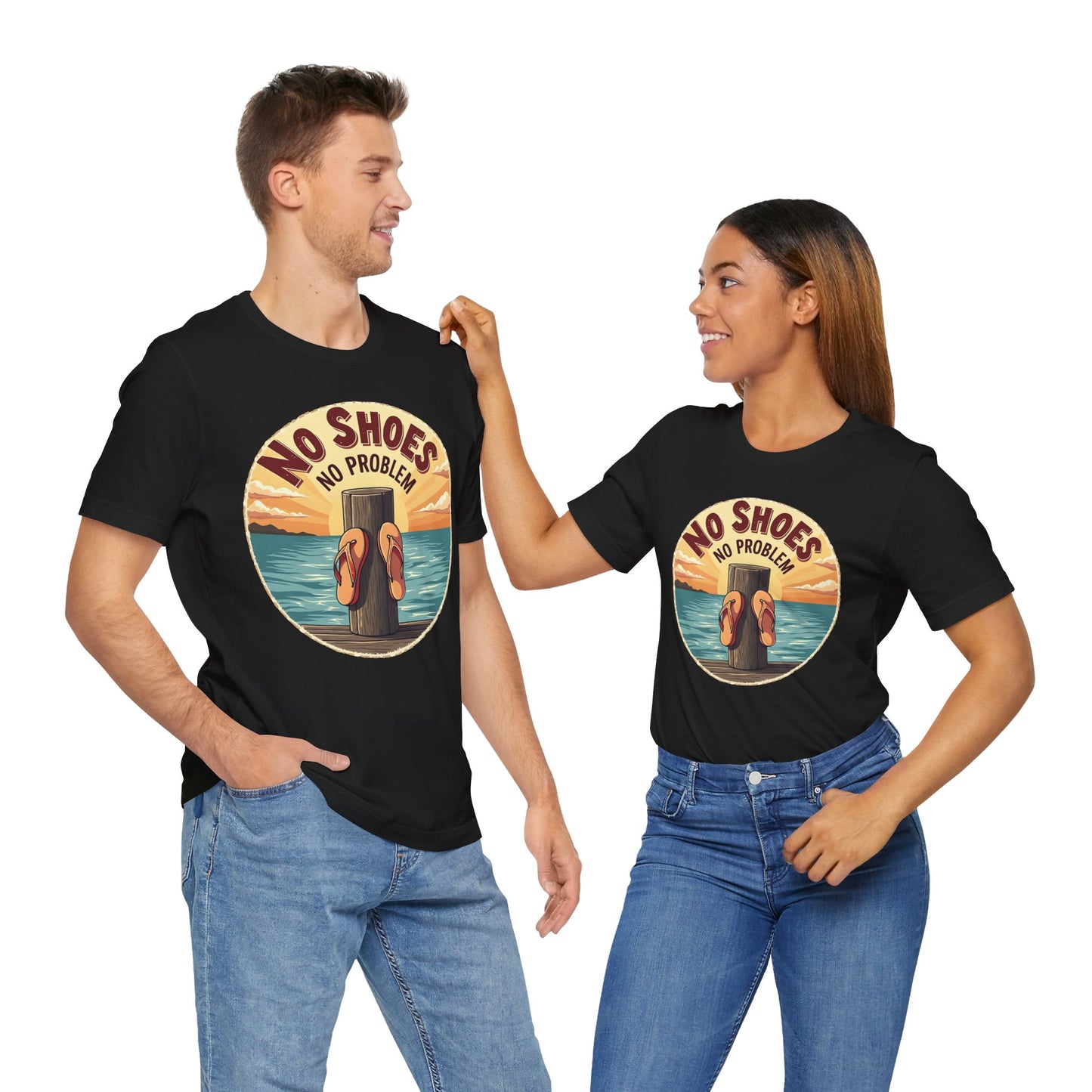 A man and woman stand side by side, smiling at each other in a plain white setting. Both wear the Unisex No Shoes No Problem Graphic Tee—a casual beach vibe shirt with bold text on the front.