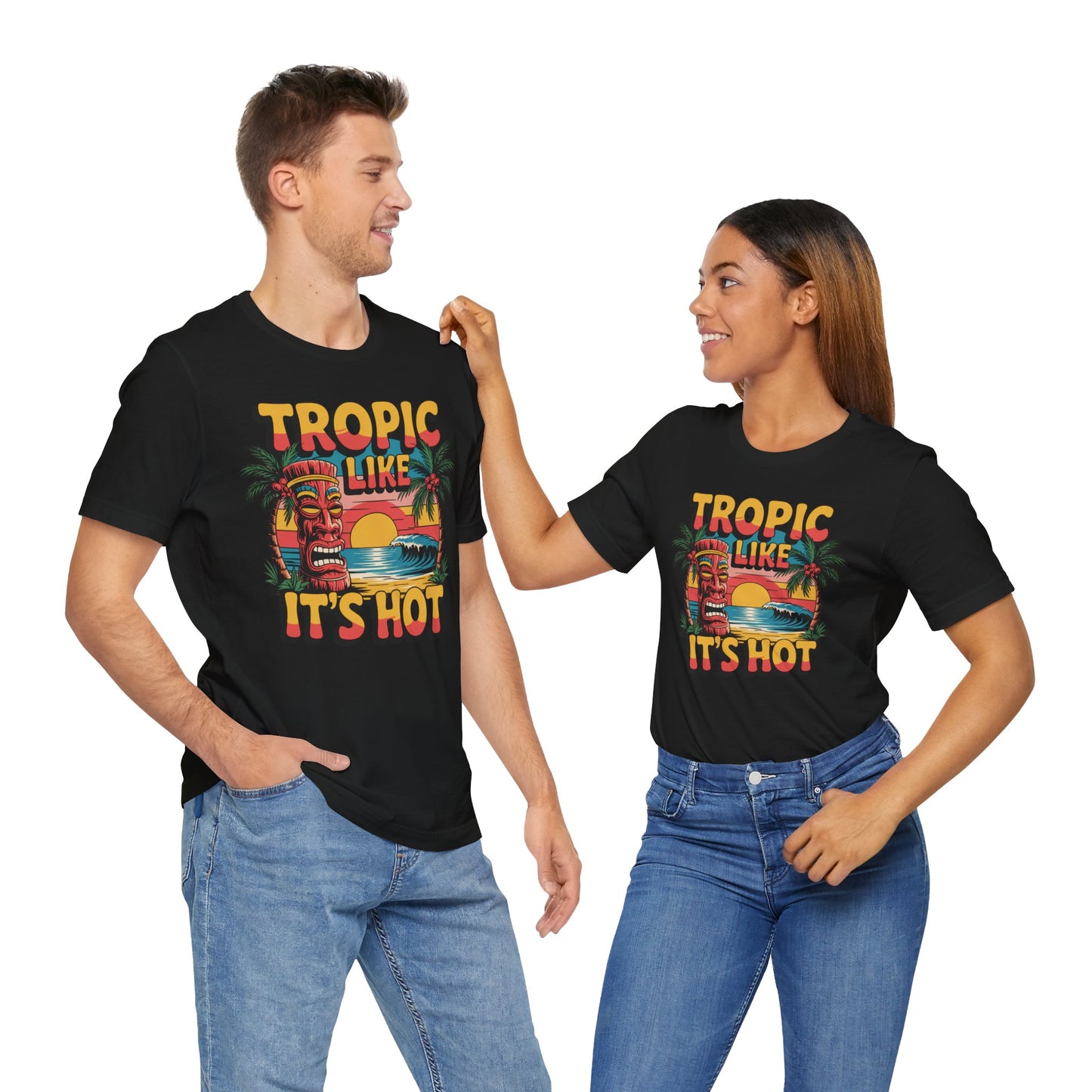 A man and woman smile, both wearing the Tropic Like Its Hot Unisex Tiki T-Shirt featuring a colorful tiki mask, palm trees, and vacation vibes—perfect with jeans for summer festivals or casual outings.
