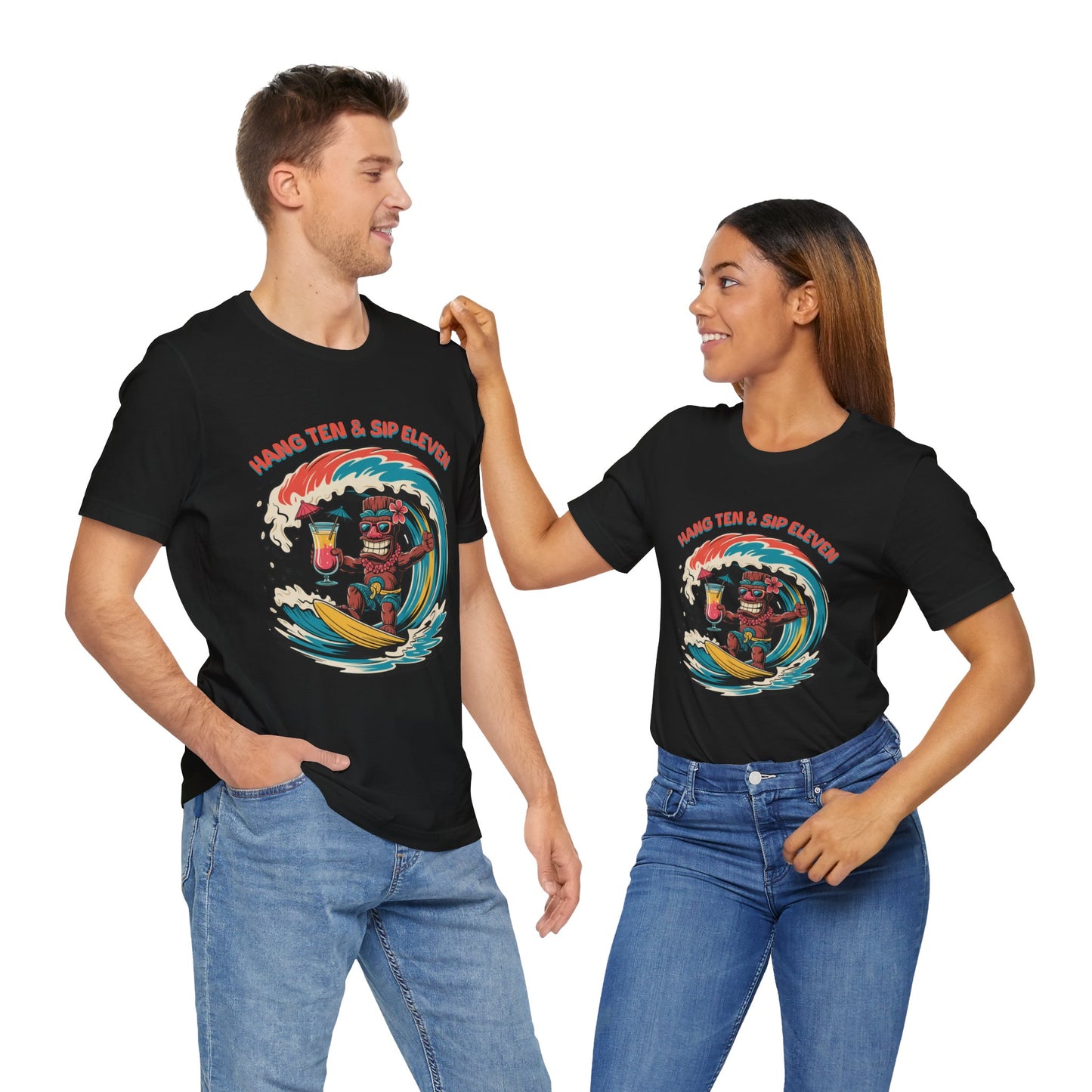 A man and woman smile at each other in matching Surf Vibe Tiki Unisex Jersey T-Shirts, featuring a colorful surf-inspired Hang Ten & Sip Eleven design. Both pose casually in jeans.