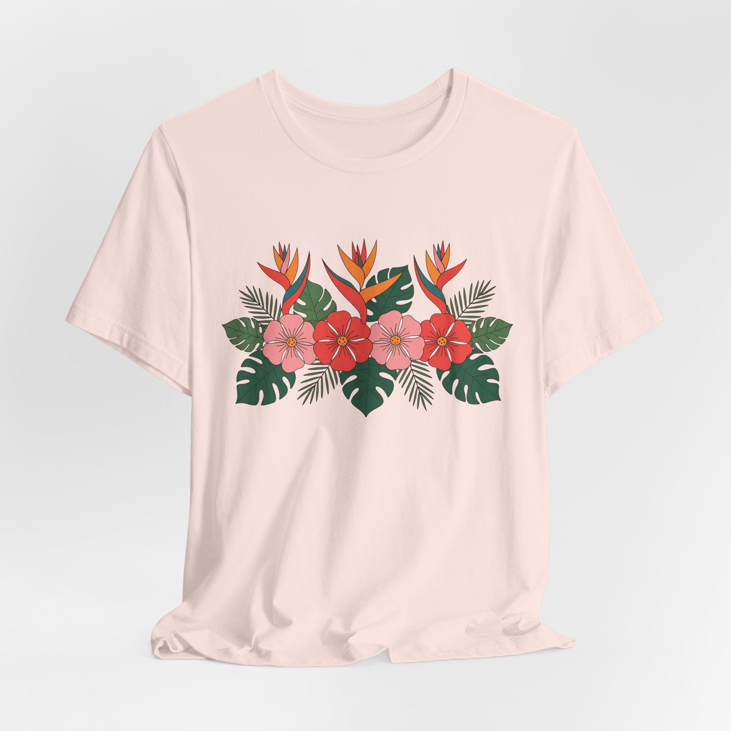 The Tropical Floral Unisex T-Shirt – Perfect for Summer Celebrations showcases a light pink base with vibrant red, pink, and orange tropical flowers and lush green leaves printed across the chest.