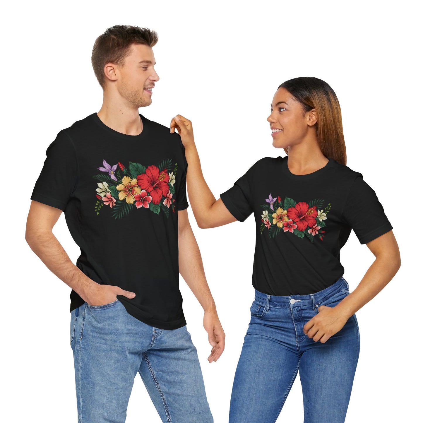 A man and a woman, both in blue jeans, smile at each other while wearing matching Tropical Floral Unisex T-Shirts – Vibrant Summer Style – featuring bold floral patterns, against a white background.