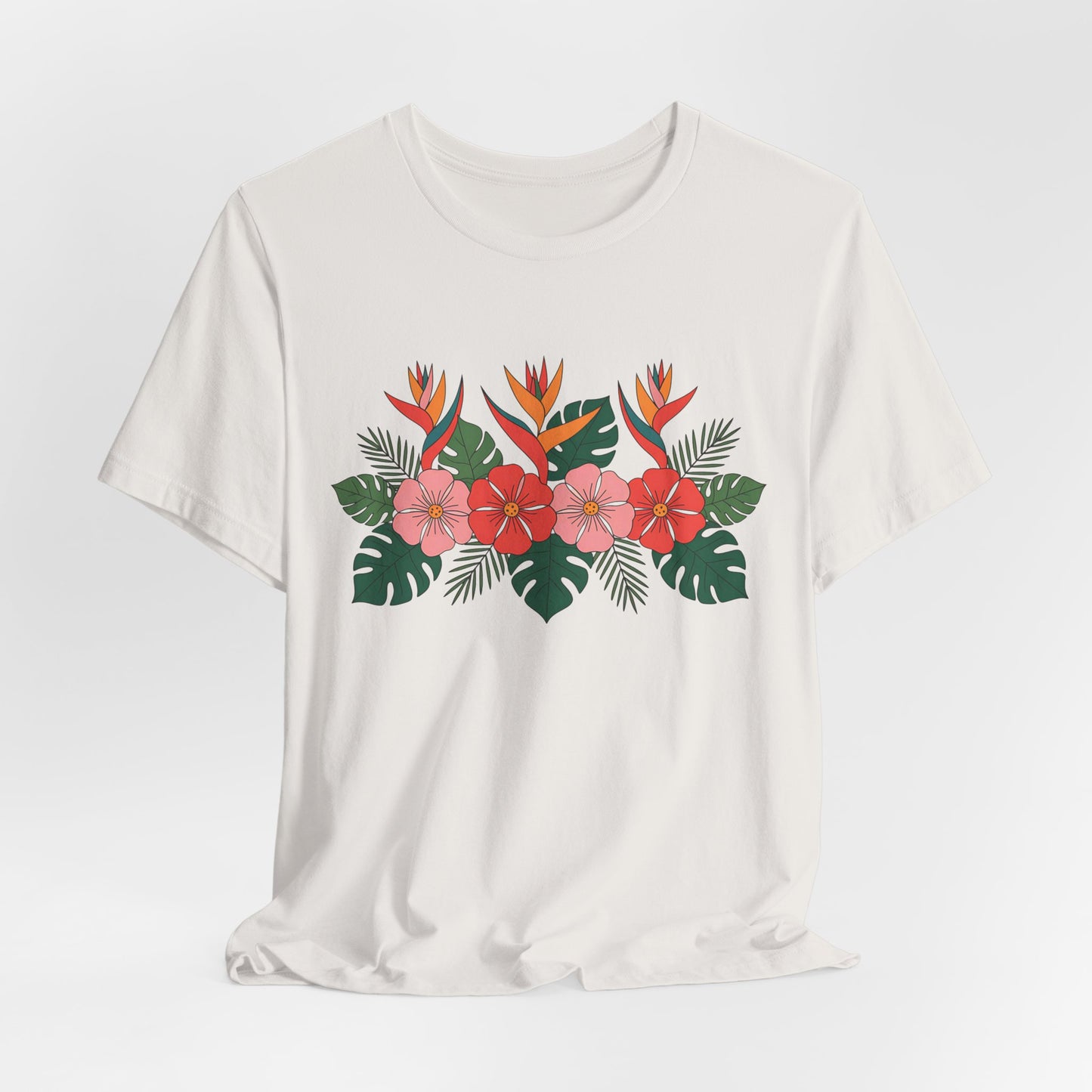 The Tropical Floral Unisex T-Shirt – Perfect for Summer Celebrations features a vibrant front print with red hibiscus, pink plumeria, orange bird of paradise flowers, and green tropical leaves on breathable jersey fabric.
