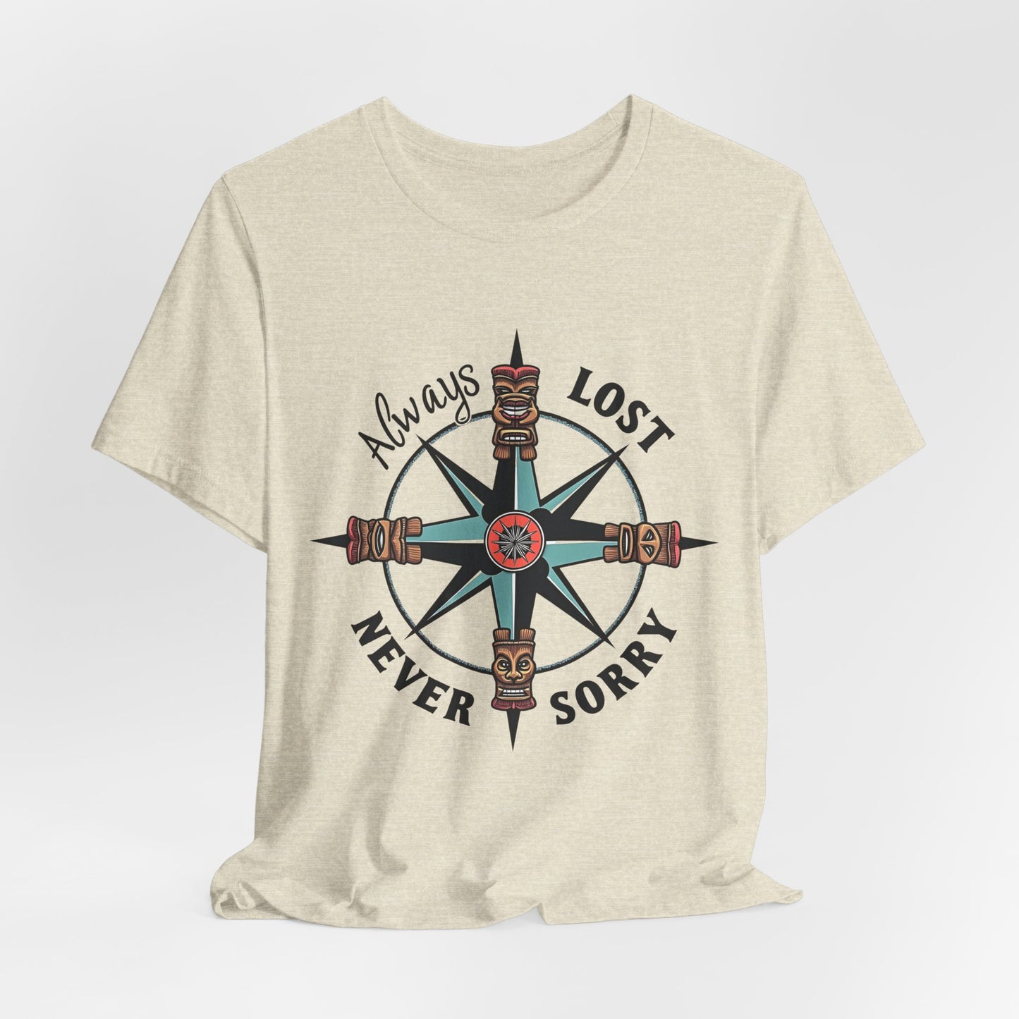 The Always Lost, Never Sorry Graphic Tee - Unisex Short Sleeve T-Shirt features a large compass with tiki faces and the phrase Always Lost Never Sorry—ideal for adventurers seeking a unique, light beige graphic tee.