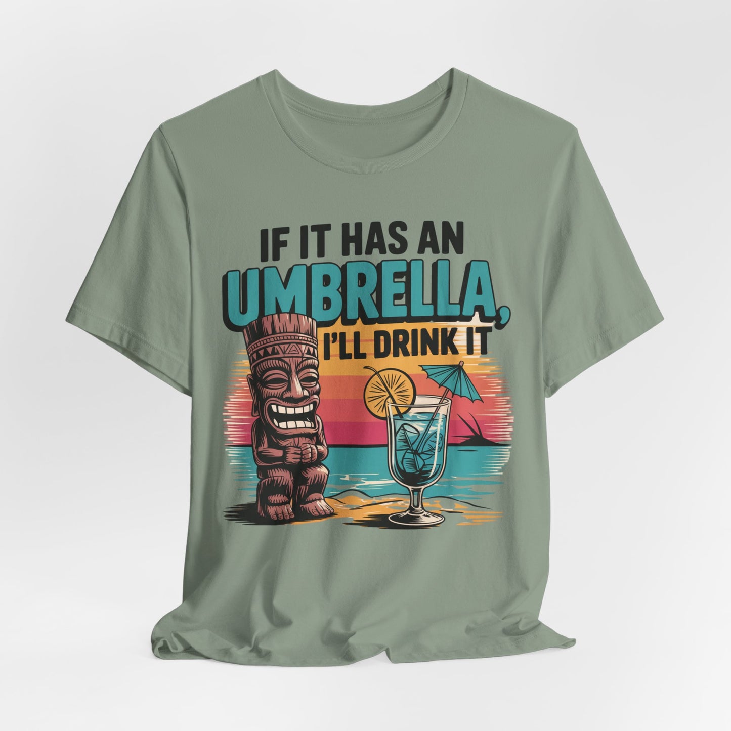The Tropical Fun Tiki T-Shirt - If It Has an Umbrella, I’ll Drink It features a sage green unisex design with tropical vibes: a tiki statue, cocktail with umbrella, sunset, and the playful quote on the front.