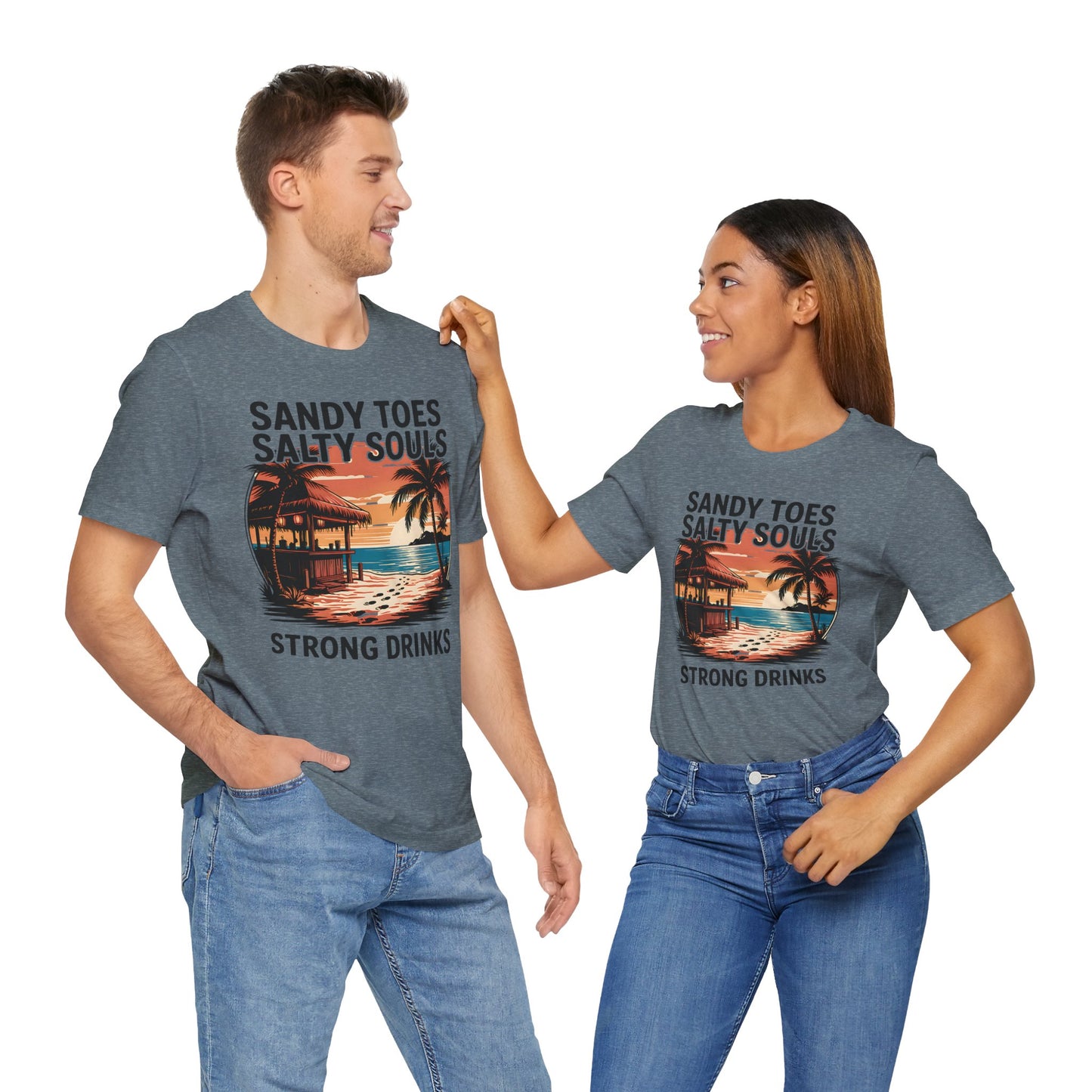A man and woman smile at each other in matching “Sandy Toes Salty Souls Tee - Unisex Jersey Short Sleeve for Beach Lovers,” featuring a vibrant tropical sunset, palm trees, and the slogan “Sandy Toes Salty Souls Strong Drinks.”.