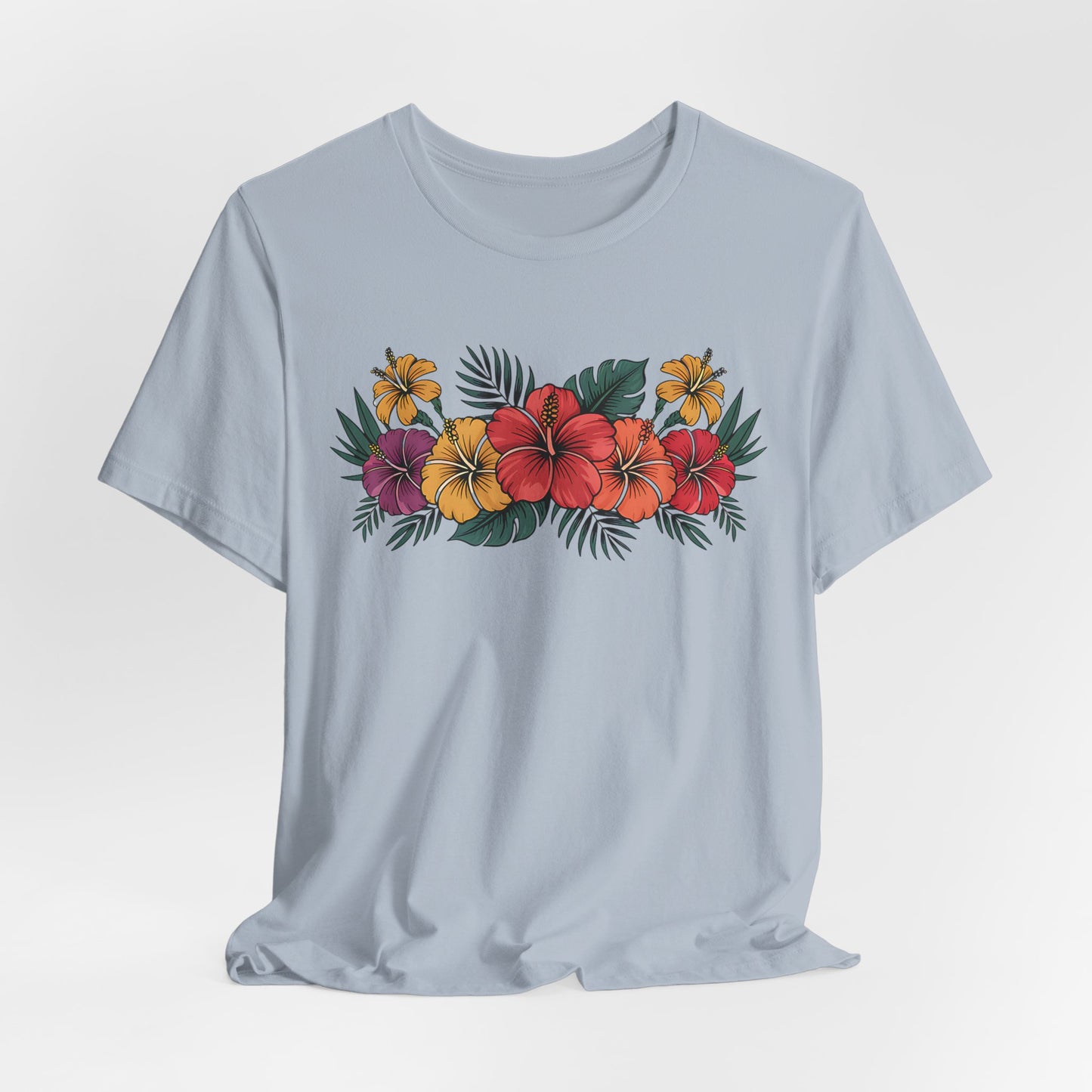 The Tropical Floral Unisex T-Shirt - Perfect for Summer Days features a vibrant red, yellow, and orange hibiscus floral design with green leaves across the chest on light blue soft Airlume cotton for all-day comfort.