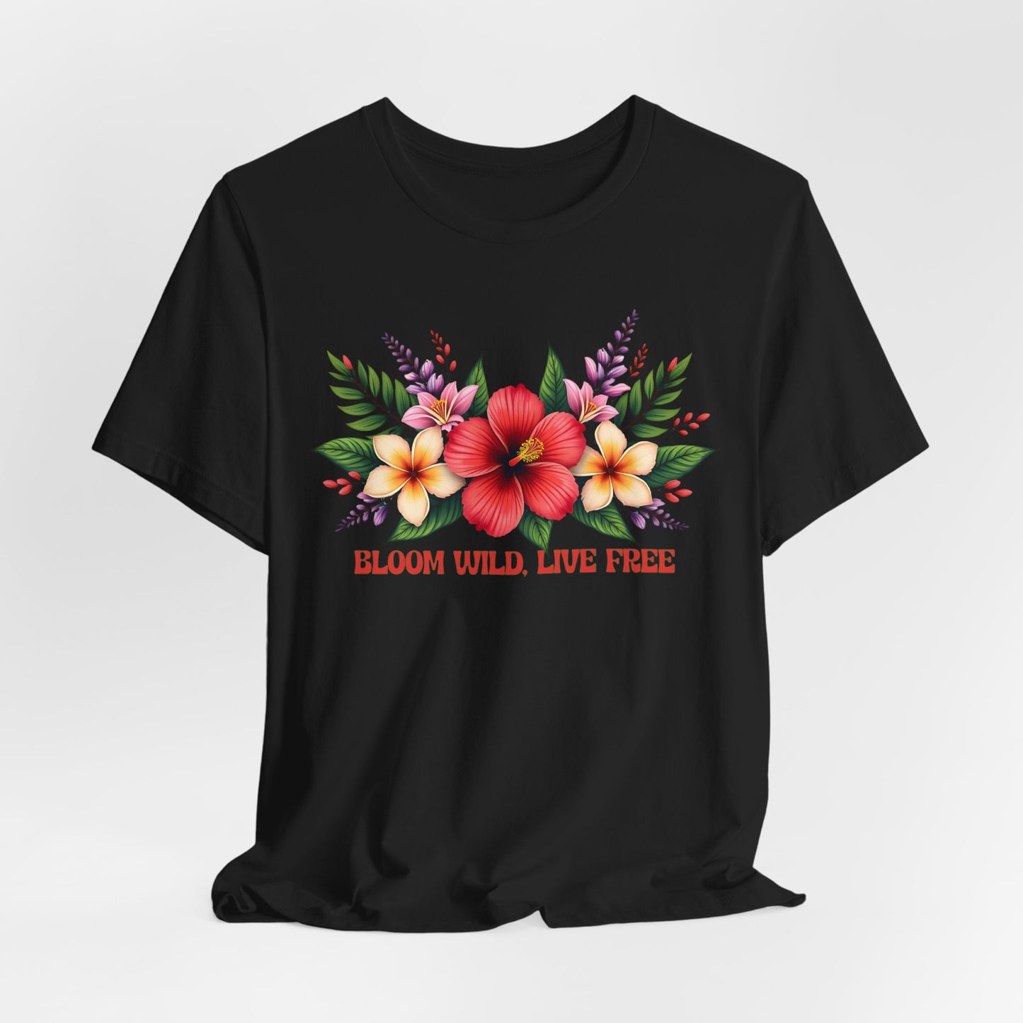 The Bloom Wild, Live Free Floral Tee is a black unisex jersey short sleeve T-shirt with hibiscus and plumeria flowers above “BLOOM WILD, LIVE FREE” in bold red and yellow. Made from soft, breathable fabric for all-day comfort.