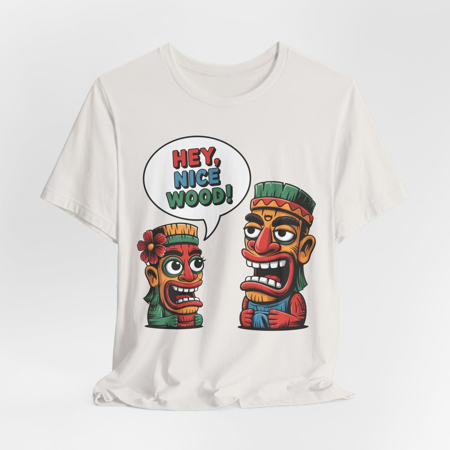 The Tropical Humor Short Sleeve Tiki T-Shirt - Hey, Nice Wood! Graphic features two vibrant cartoon tiki faces on a white unisex jersey tee. The left tiki has a flower and faces the right one, who says, HEY, NICE WOOD! in a playful speech bubble.