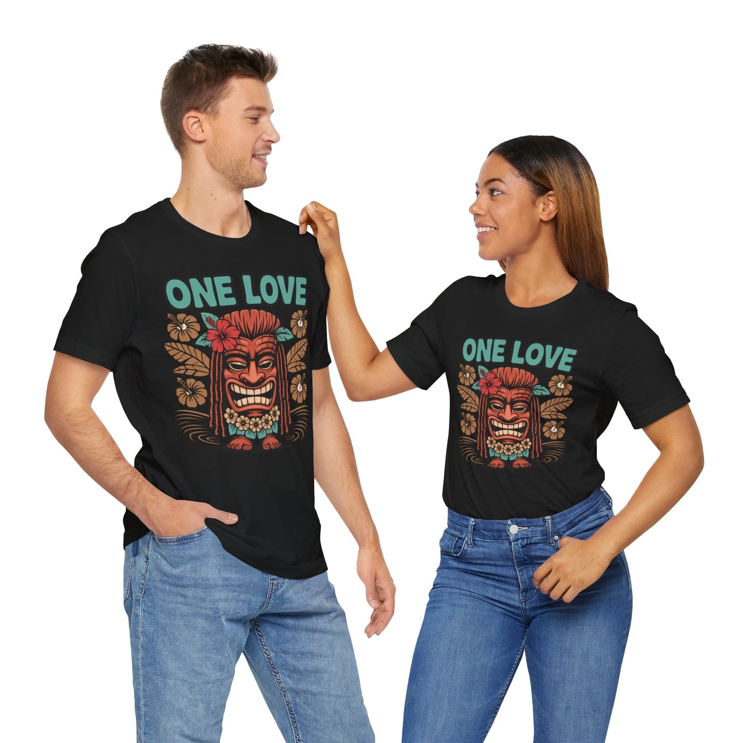 A smiling couple in blue jeans stand against a white background wearing matching One Love Tropical Unisex Jersey Tiki T-Shirts—Vibrant Beach Vibe Shirts with colorful tiki masks and tropical leaves, perfect for beach lovers or festivals.