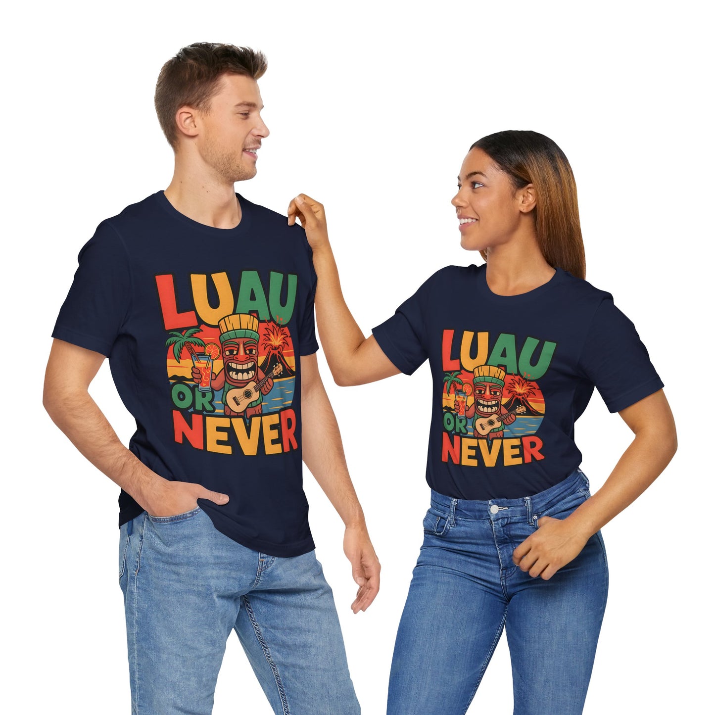 A smiling couple in matching navy blue Tropical Luau Short Sleeve Tiki T-Shirts—featuring LUAU OR NEVER and colorful tiki and flower graphics—radiate tropical vibes. The woman touches the mans shoulder, both wearing jeans. Perfect for summer celebrations!.