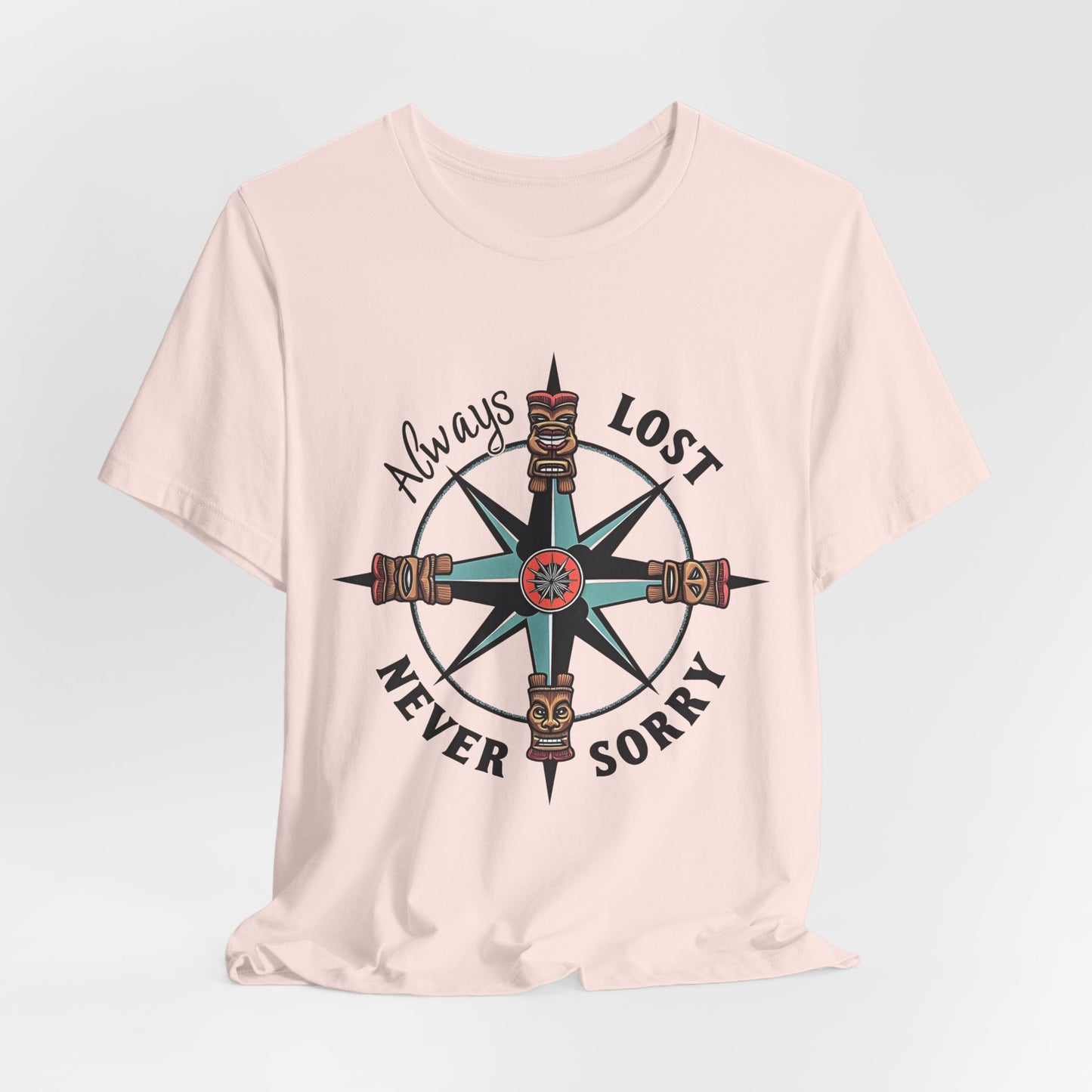 The Always Lost, Never Sorry Graphic Tee is a beige unisex short sleeve shirt with a compass and tiki faces design. Always Lost, Never Sorry circles the graphic in a playful font, capturing an adventurous spirit.