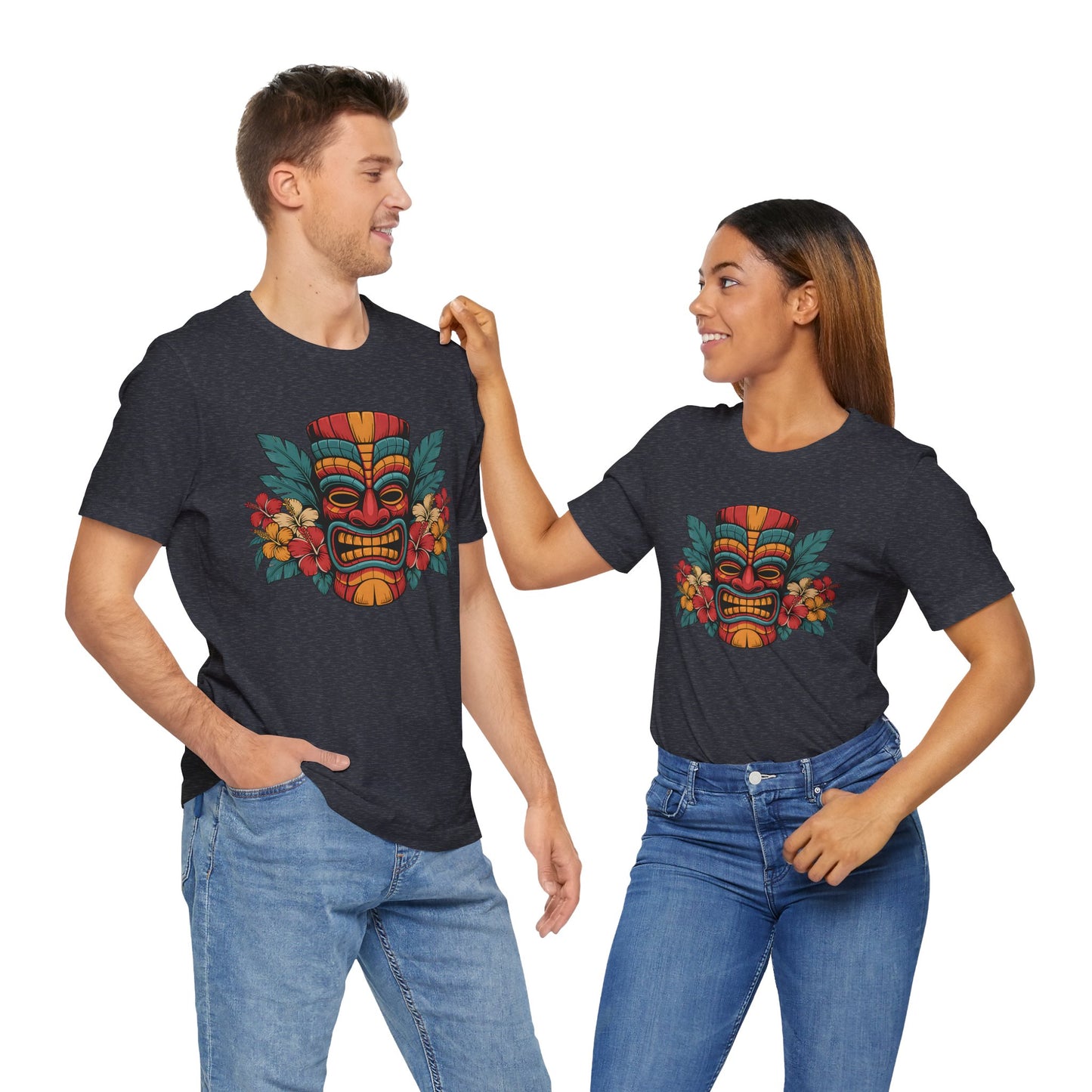 A man and woman smile at each other in matching Tropical Tiki Mask T-Shirt - Unisex Jersey Short Sleeves, featuring a vibrant tiki mask and floral design. The man has one hand in his pocket as the woman touches his shoulder.