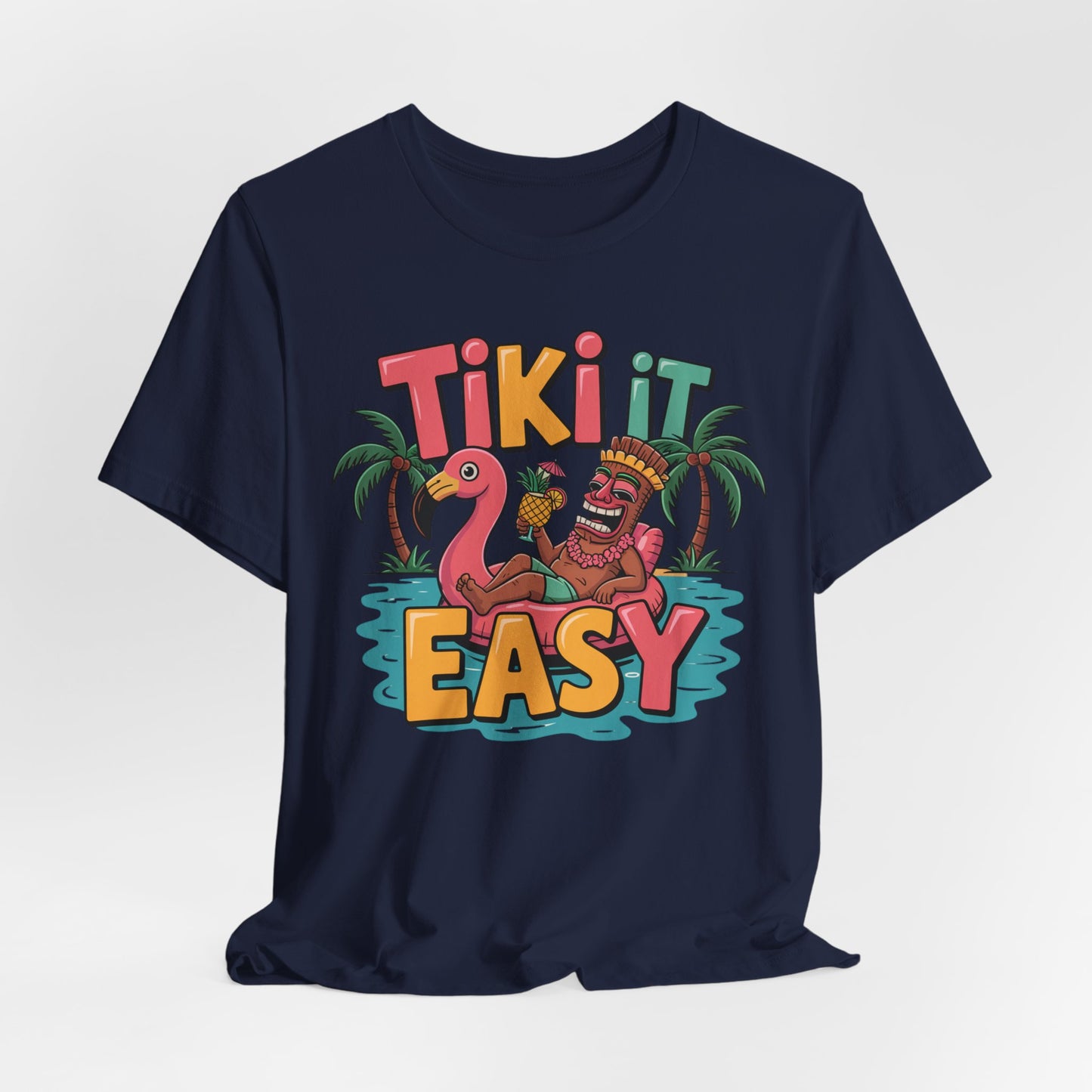 The Tiki It Easy Unisex Short Sleeve Tiki T-Shirt brings tropical beach vibes with a playful tiki statue on a pink flamingo float, palm trees, and bold Tiki It Easy lettering for a fun Hawaiian-themed look.