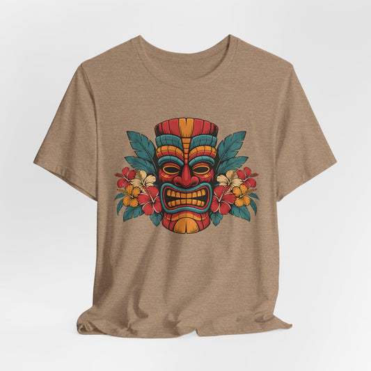 The Tropical Tiki Mask T-Shirt - Unisex Jersey Short Sleeve in tan features a vibrant central Tiki mask with tropical flowers and green leaves, delivering a fun island vibe in breathable fabric for all-day comfort.