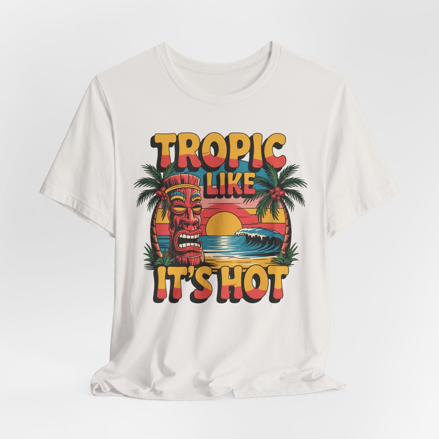 The Tropic Like Its Hot Unisex Tiki T-Shirt features a vibrant tropical design with a tiki mask, palm trees, sunset, and TROPIC LIKE ITS HOT—perfect for festivals or vacation vibes.