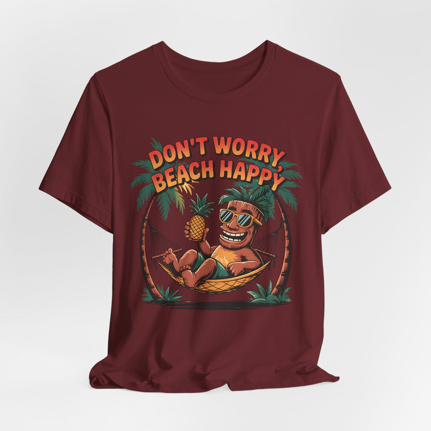 The Dont Worry Beach Happy Tiki T-Shirt is a maroon unisex jersey tee with a cartoon coconut in sunglasses relaxing in a hammock with a pineapple and DONT WORRY, BEACH HAPPY above—ideal for beach lovers and summer vibes.