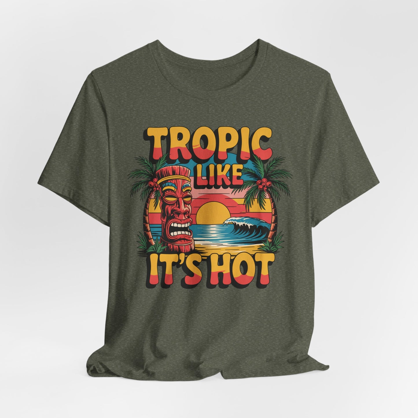 The Tropic Like It’s Hot Unisex Tiki T-Shirt features a tiki mask, palm trees, ocean waves, and a sunset with “Tropic like it’s hot” text—perfect for beach days or summer festivals. Fun vacation vibes tee for everyone!.