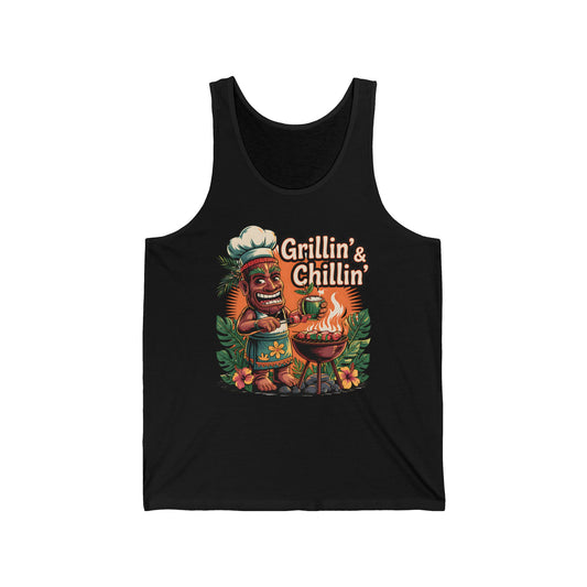 The Grillin & Chillin Unisex Jersey Tiki Tank Top features a vibrant cartoon tiki chef grilling amid tropical leaves—perfect for summer BBQs and parties.
