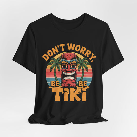The Tiki Vibes Unisex Jersey Tiki T-Shirt features a colorful tiki mask, palm trees, sunset background, and bold Dont Worry, Be Tiki text—perfect for adding tropical flair to your casual look.