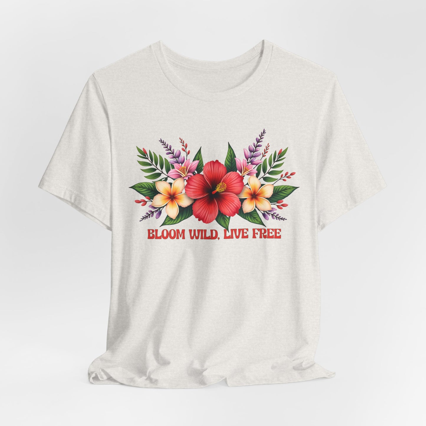 The Bloom Wild, Live Free Floral Tee is a light-colored unisex jersey short sleeve T-shirt featuring bold red “BLOOM WILD, LIVE FREE” text below vibrant red, yellow, and pink flowers with green leaves.