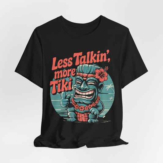 The Tiki Vibes Graphic Tiki T-Shirt - Less Talkin, More Tiki Unisex Shirt is a black tee featuring a colorful cartoon tiki with a flower, giving a thumbs up and “Less Talkin’, More Tiki” in bold orange on a vivid tropical background.