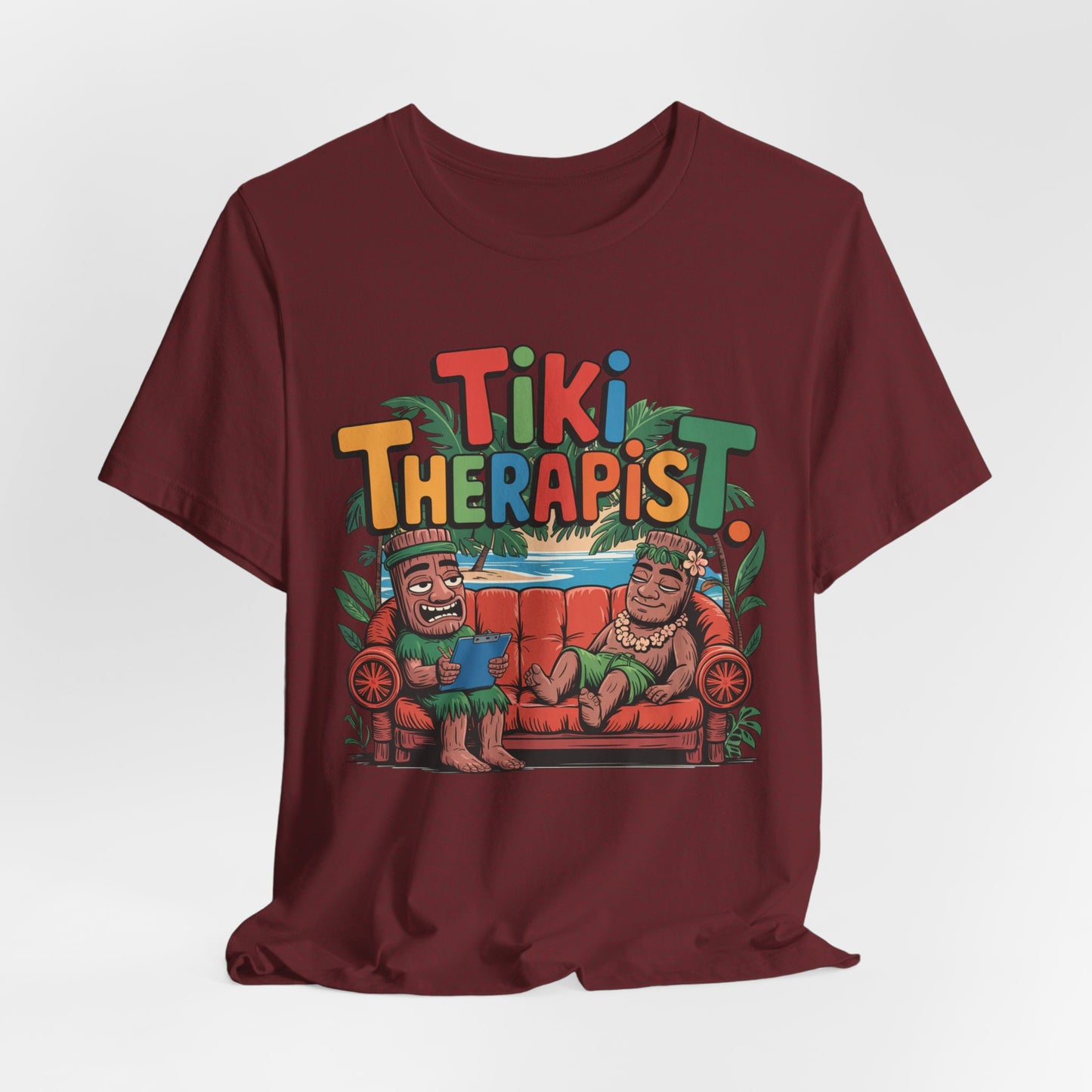 The Tiki Therapist Unisex Tiki T-Shirt is a maroon, breathable cotton tee with two smiling tiki figures on a couch, vibrant Tiki Therapist text, and lush green leaves—perfect for beach lovers seeking a fun, tropical Hawaiian vibe.