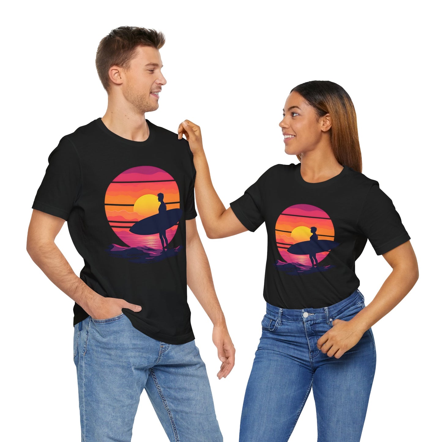 A man and woman in jeans, beach lovers, stand side by side smiling in matching Sunset Surfing Unisex Jersey T-Shirts—featuring a sunset and surfer graphic printed with DTG for vibrant color.