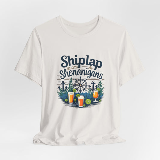 The Shiplap Shenanigans Unisex Short Sleeve Tee is crafted from soft Airlume cotton and features a nautical Shiplap Shots & Shenanigans design with anchors, ship wheel, pine branches, lime wedges, and three beer glasses—ideal for brewery lovers.
