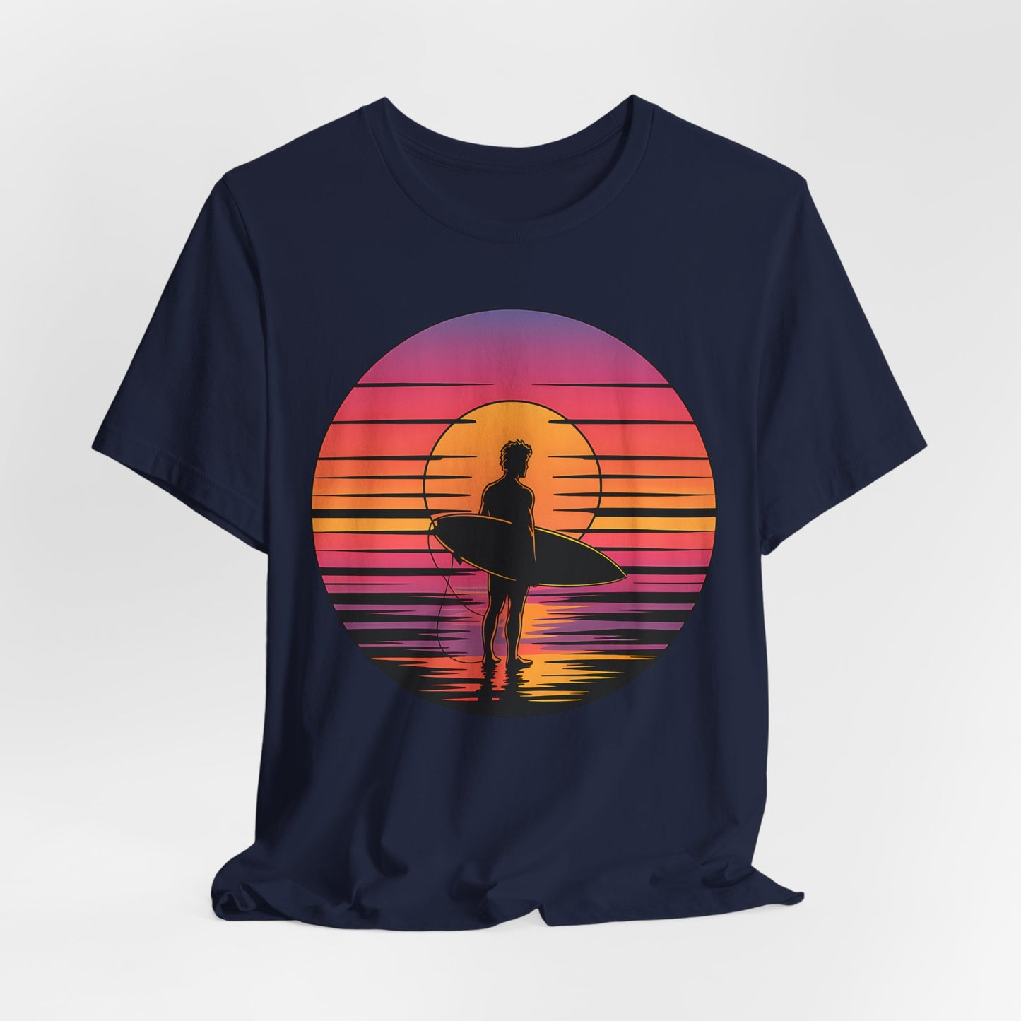 The Retro Surfing Unisex Jersey T-Shirt - Sunset Vibes in navy features a silhouette with a surfboard by the water and a vibrant sunset in pink, orange, and yellow on soft Airlume combed and ring-spun cotton.