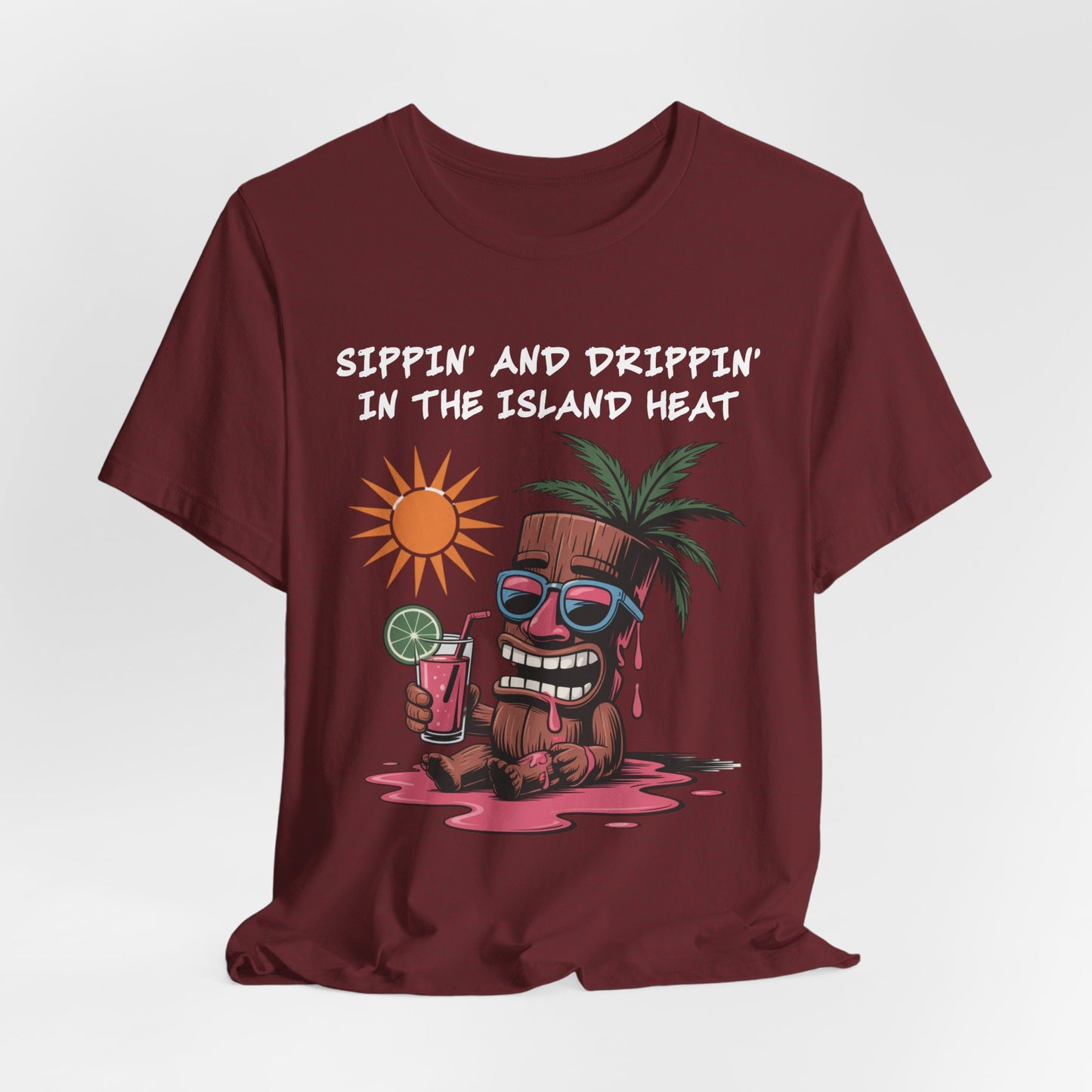 The Tropical Vibes Tiki T-Shirt – Sippin’ and Drippin’ in the Island Heat features a cartoon tiki with sunglasses, relaxing in juice under the sun for the ultimate island vibe.