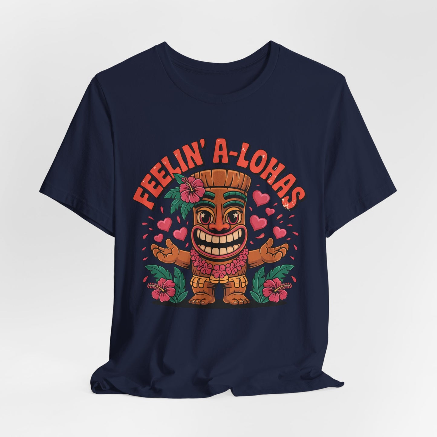 The Feelin A-Lohas Unisex Jersey Tiki T-Shirt features a smiling tiki with outstretched arms, pink hearts and flowers, plus FEELIN A-LOHAS in orange text—a vibrant, tropical graphic shirt perfect for casual wear.