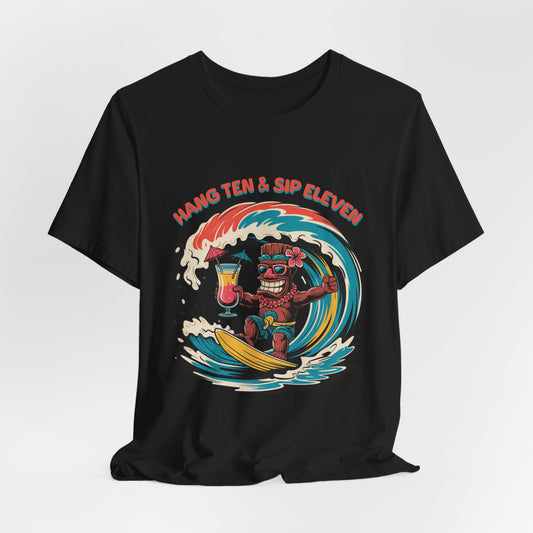 The Surf Vibe Tiki T-Shirt - Hang Ten & Sip Eleven Unisex Jersey Short Sleeve features a black, surf-inspired cartoon tiki surfing with drinks and the phrase above. Made from breathable cotton for all-day comfort.