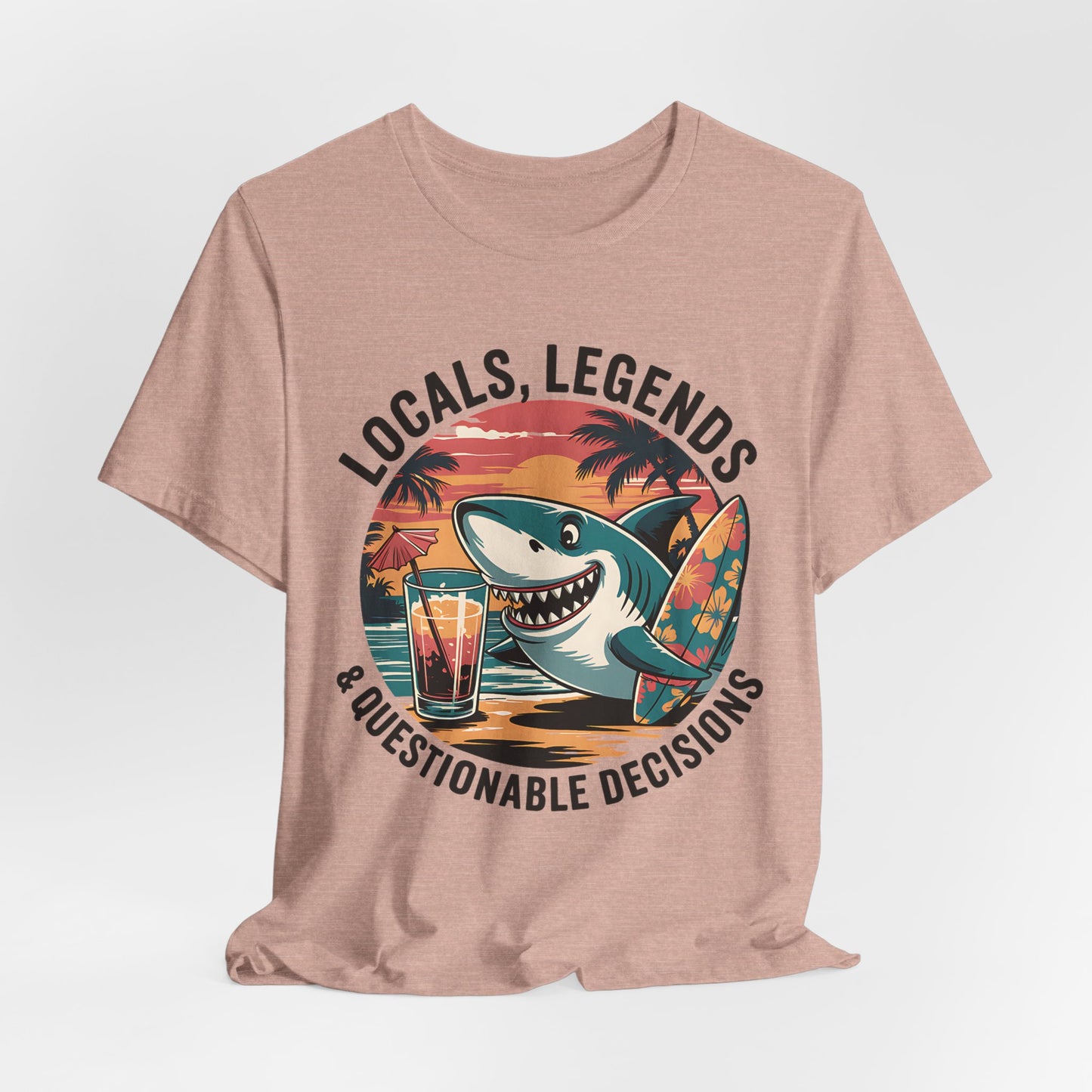 The Funny Shark Graphic T-Shirt - Locals, Legends & Questionable Decisions is a tan unisex tee with a cartoon shark holding a surfboard and drink, radiating sunset beach vibes—perfect for beach lovers.