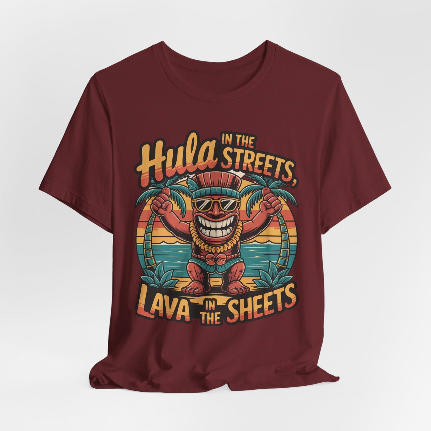 The Hula in the Streets Short Sleeve Tiki T-Shirt is a maroon unisex tee with a cartoon tiki in sunglasses and a grass skirt between palm trees, plus “Hula in the streets, lava in the sheets”—a fun tropical pick for summer celebrations.