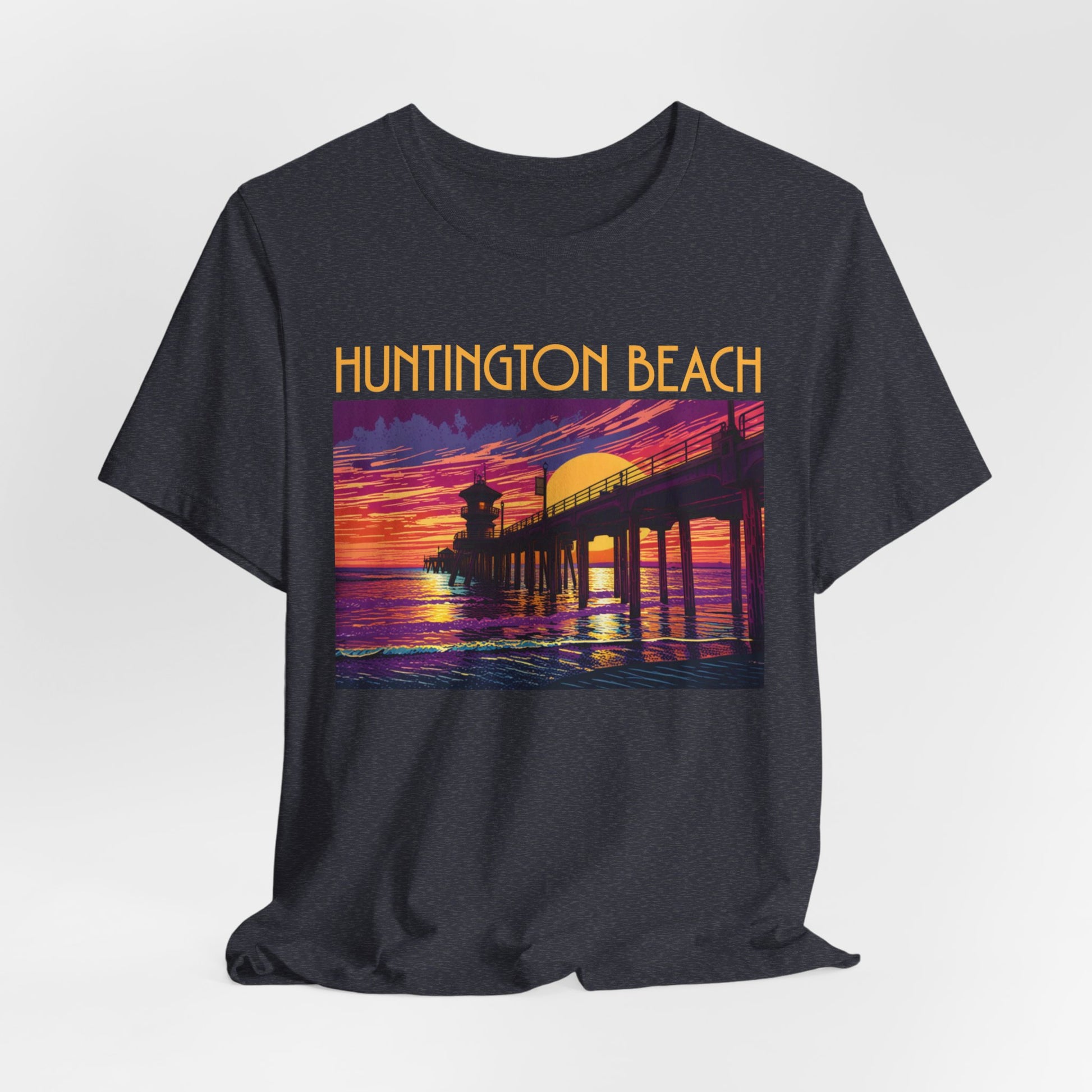 The Huntington Beach Sunset T-Shirt - Unisex Jersey Short Sleeve T-Shirt features a colorful pier-at-sunset graphic with Huntington Beach above, in vibrant orange, purple, and yellow tones celebrating beach culture.
