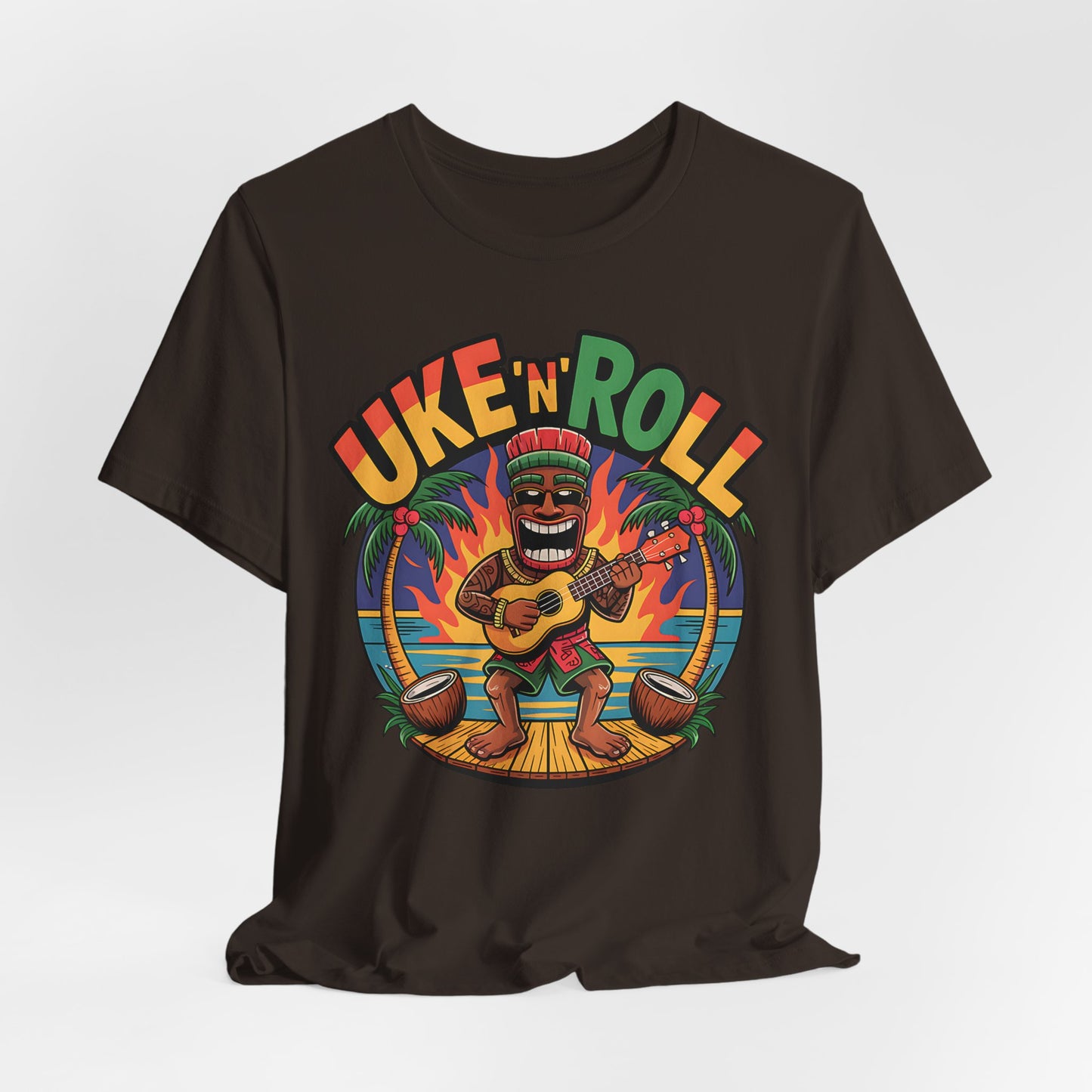 The Uke n Roll Unisex Jersey Tiki T-Shirt features a fun cartoon of a smiling man playing ukulele with palm trees and sunset, plus “UKE N ROLL” in bold colors—perfect for music lovers and beach vibes.