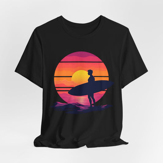 The Sunset Surfing Unisex Jersey T-Shirt features a vibrant graphic of a surfer with a surfboard at sunset in bold yellow, orange, pink, and purple—brought to life with premium DTG printing. Perfect for beach lovers.