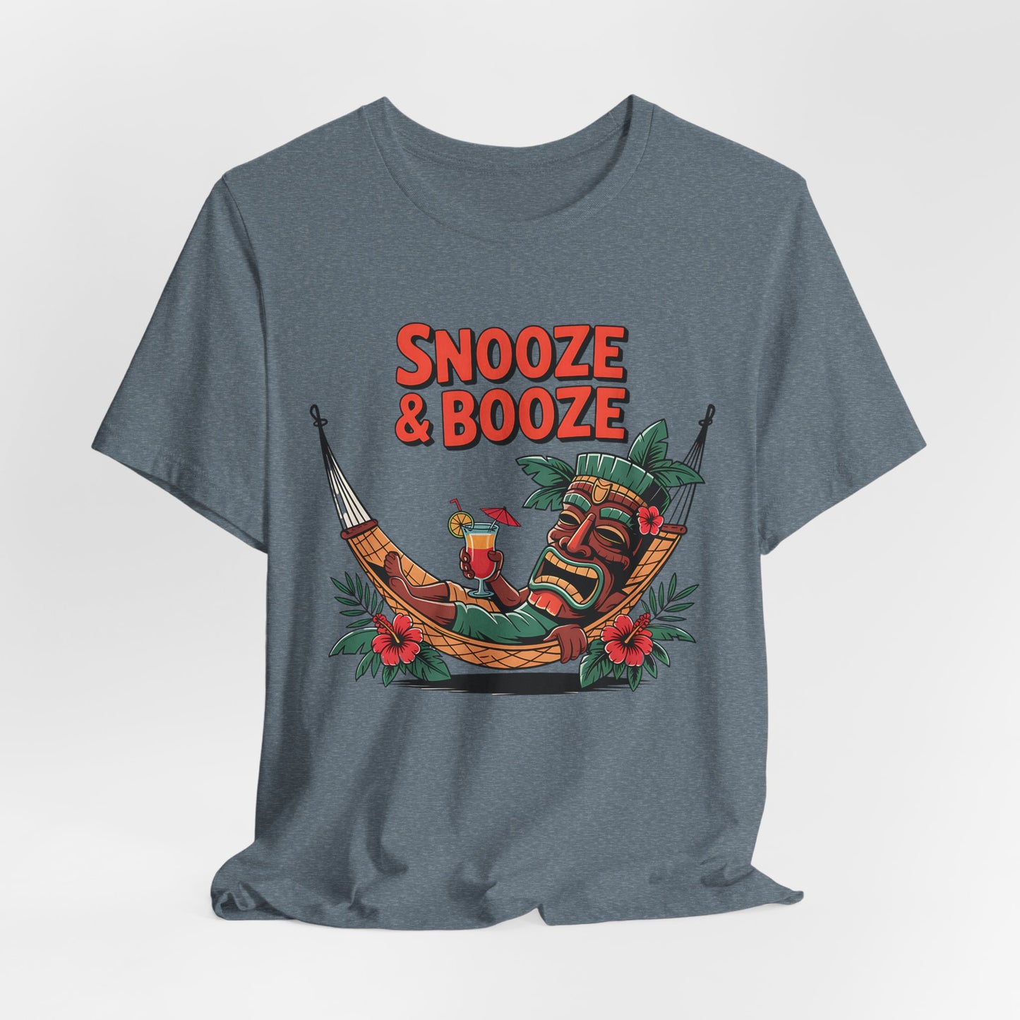 Bring tropical vacation vibes to your style with the Snooze & Booze Unisex Jersey Tiki T-Shirt—a gray tee showcasing a colorful tiki mask lounging in a hammock with a drink and bold Snooze & Booze text above.