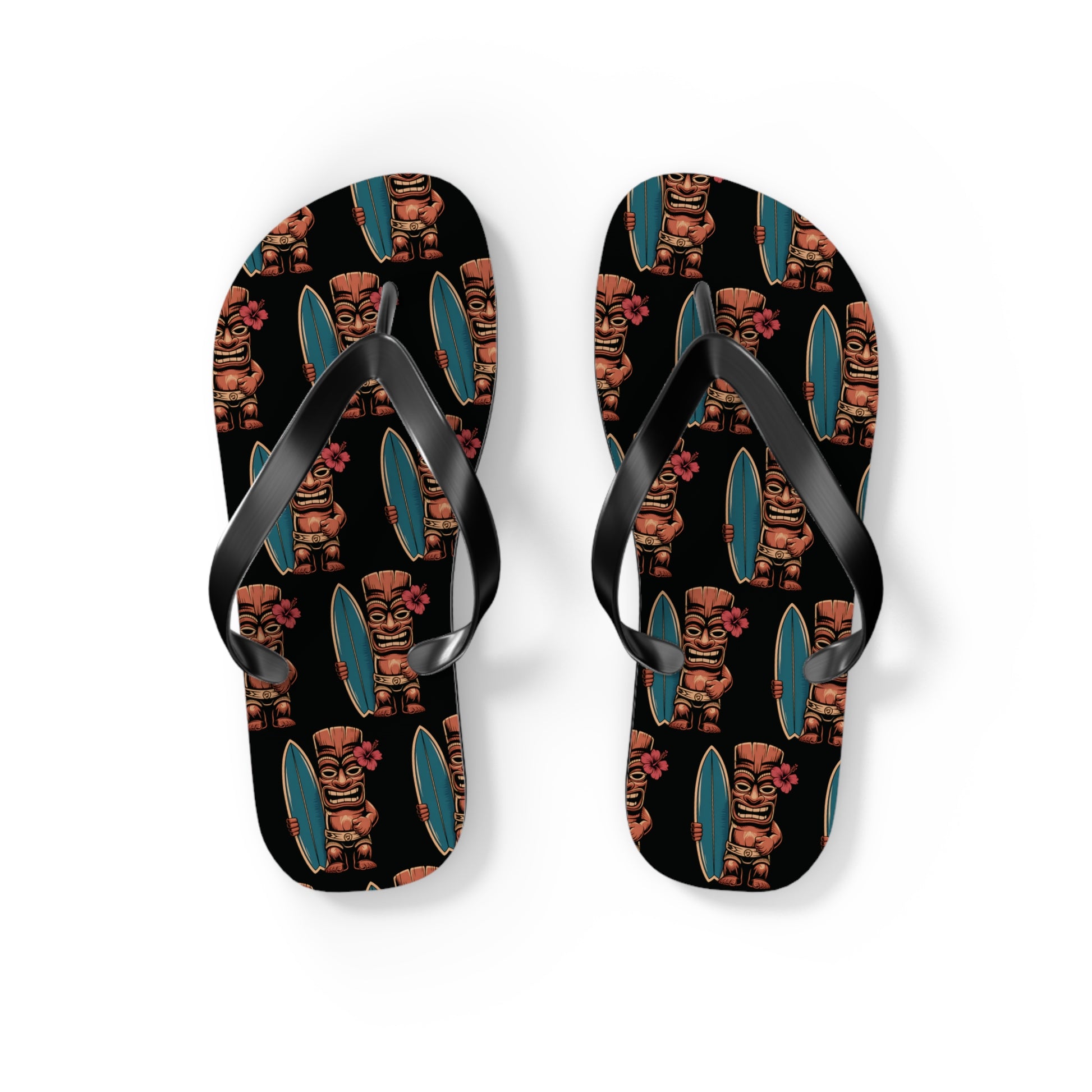 The Tiki Surf Flip Flops - Fun Summer Beach Sandals feature black soles with colorful tiki statue, surfboard, and pink flower prints, shown from above on a white background.
