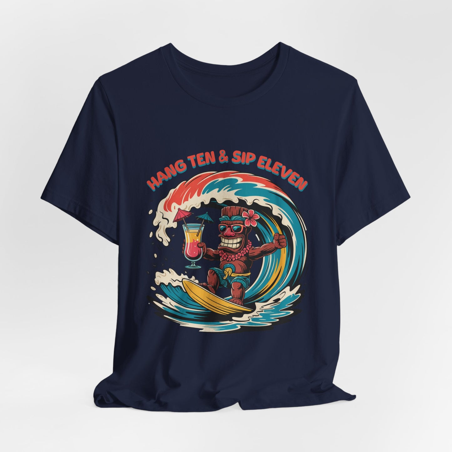 The Surf Vibe Tiki T-Shirt – Hang Ten & Sip Eleven Unisex Jersey Short Sleeve features a navy blue cotton fabric with a cartoon Tiki surfing a wave, two cocktails, and bold retro text above the design.