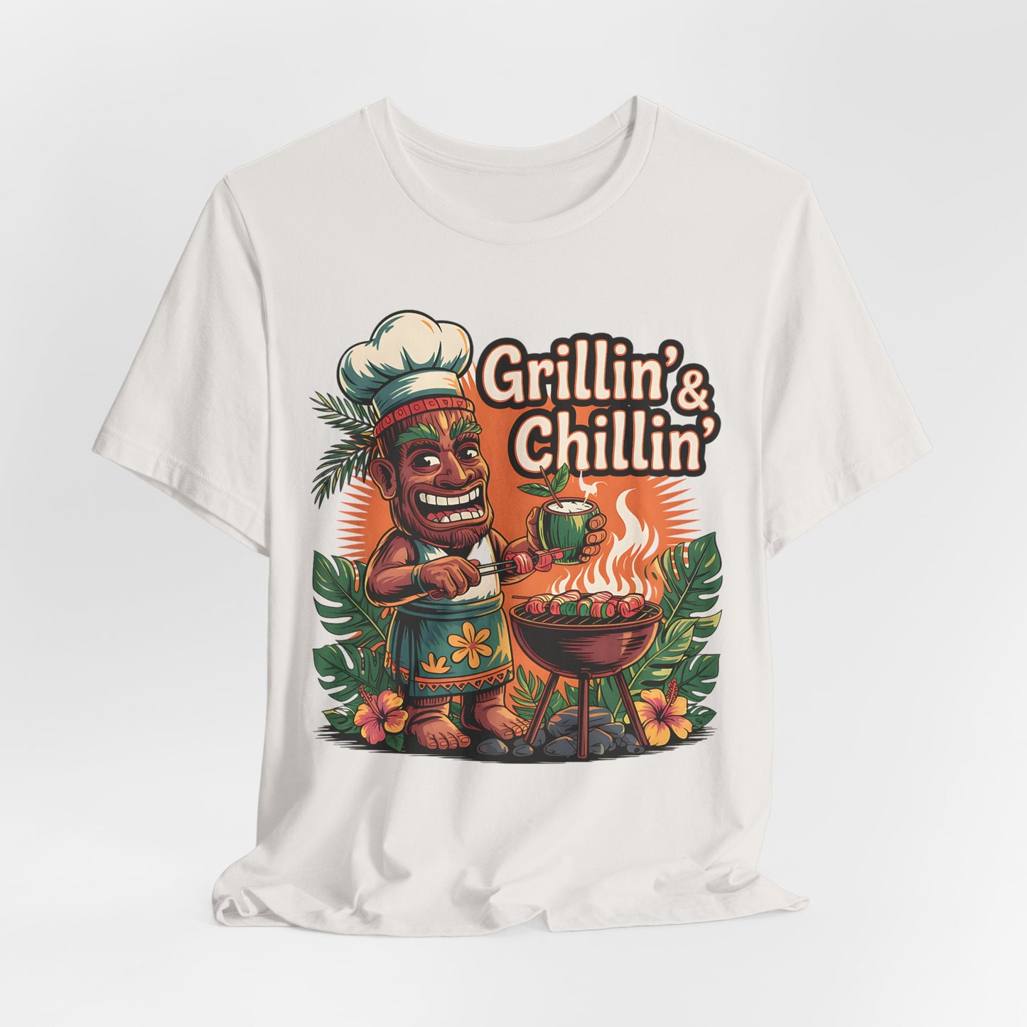 The Grilln & Chilln Unisex Jersey Tiki T-shirt features a cartoon tiki in a chef hat grilling, with tropical leaves and flowers, plus “Grillin’ & Chillin’” text—ideal for Summer BBQs or Luau Parties.